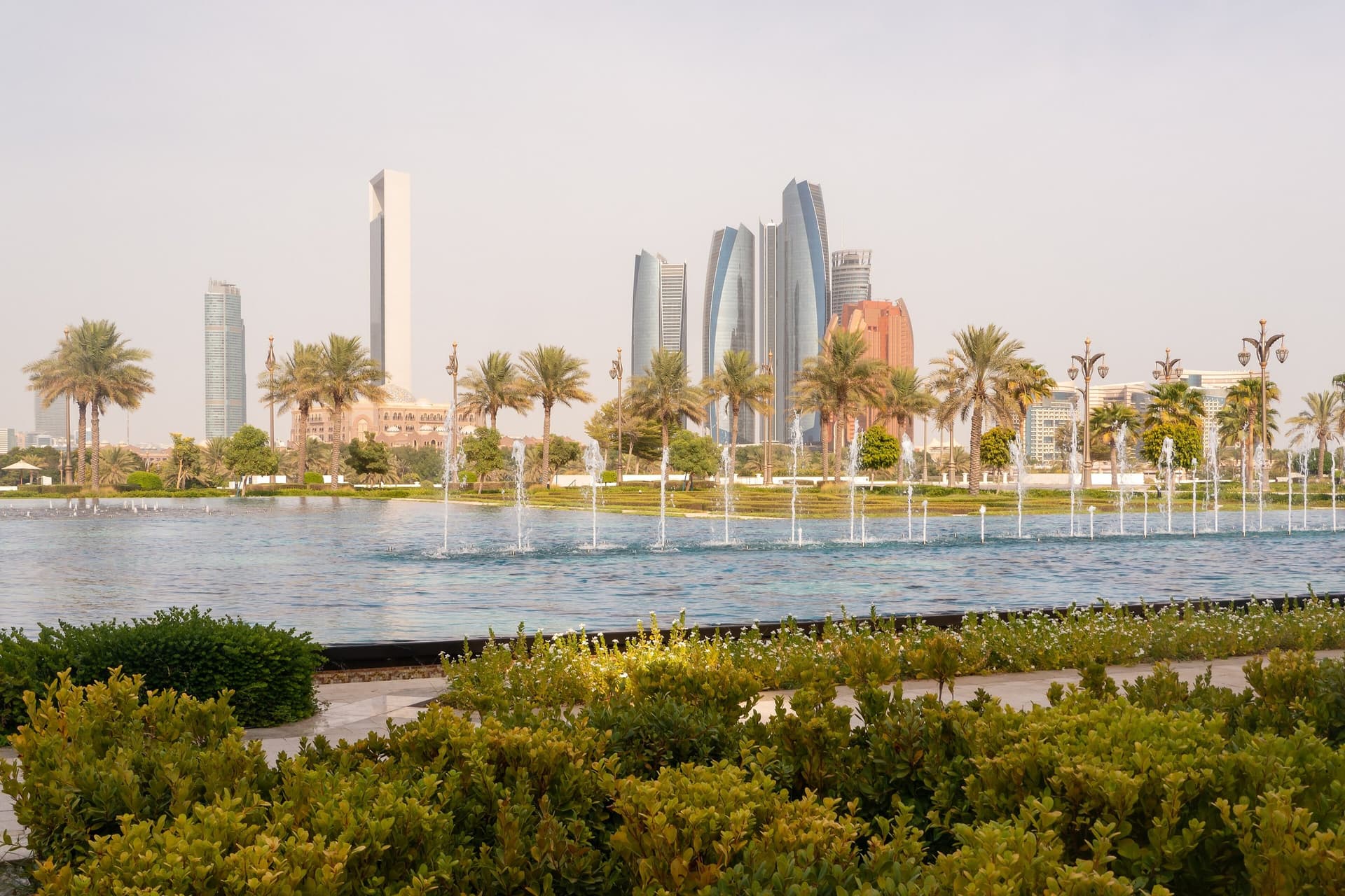 Fonteinen en palmen bij Qasr Al Watan met de torens van Abu Dhabi op de achtergrond
