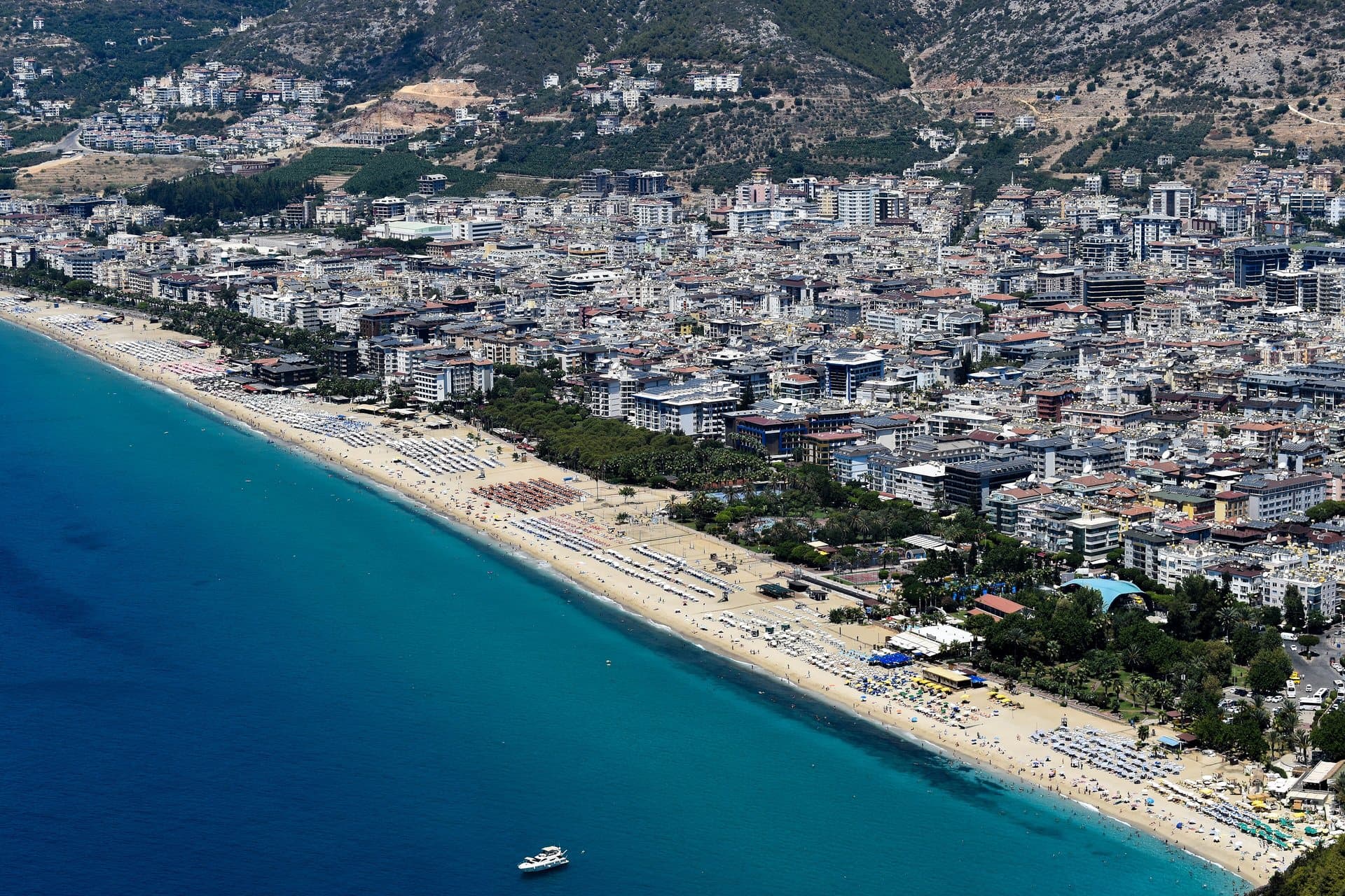 Luchtfoto van het Kleopatra-strand in Alanya: een lange zandboog langs turquoise water, met daarachter de hotels en appartementen van de stad tegen de heuvels