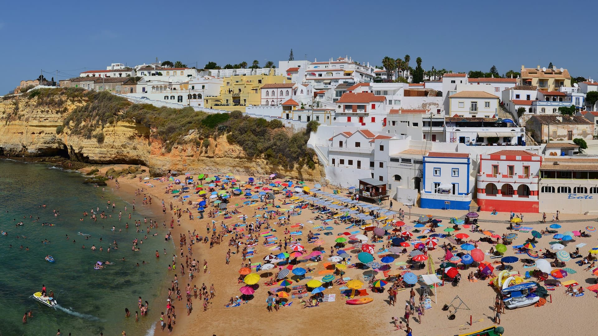 Het strand van Carvoreiro in de Algarve vol kleurige parasols, met witte huizen boven op de goudgele kliffen