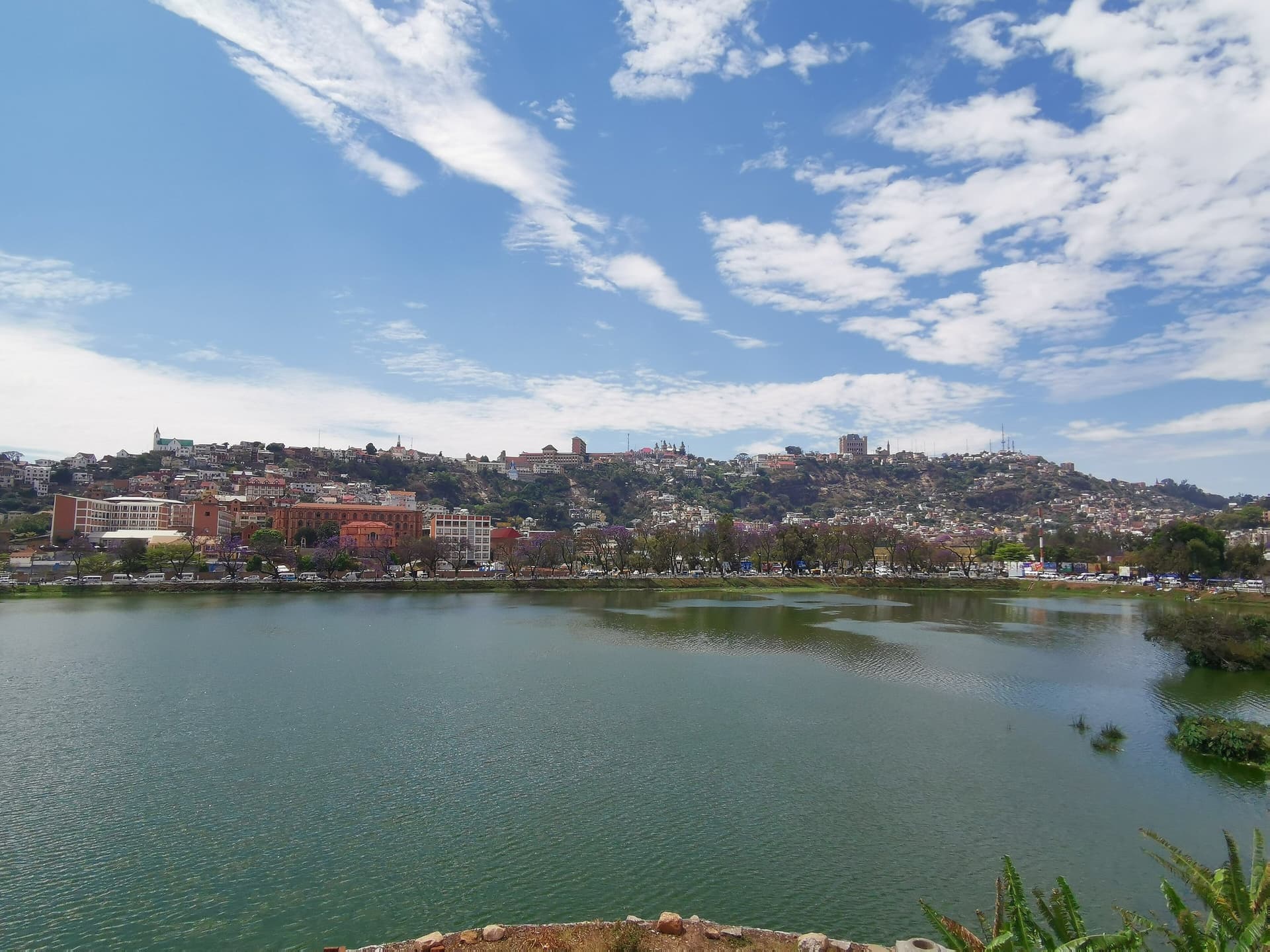 Het Anosymeer in Antananarivo onder een blauwe lucht met sluierwolken, met de heuvels van de oude stad op de achtergrond