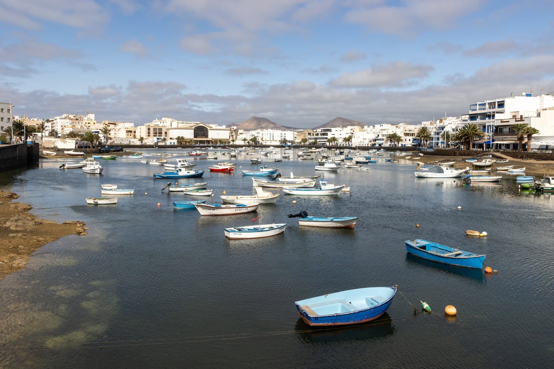 De lagune Charco de San Ginés in Arrecife op Lanzarote, vol kleine vissersbootjes, met witte huizen en vulkanen op de achtergrond