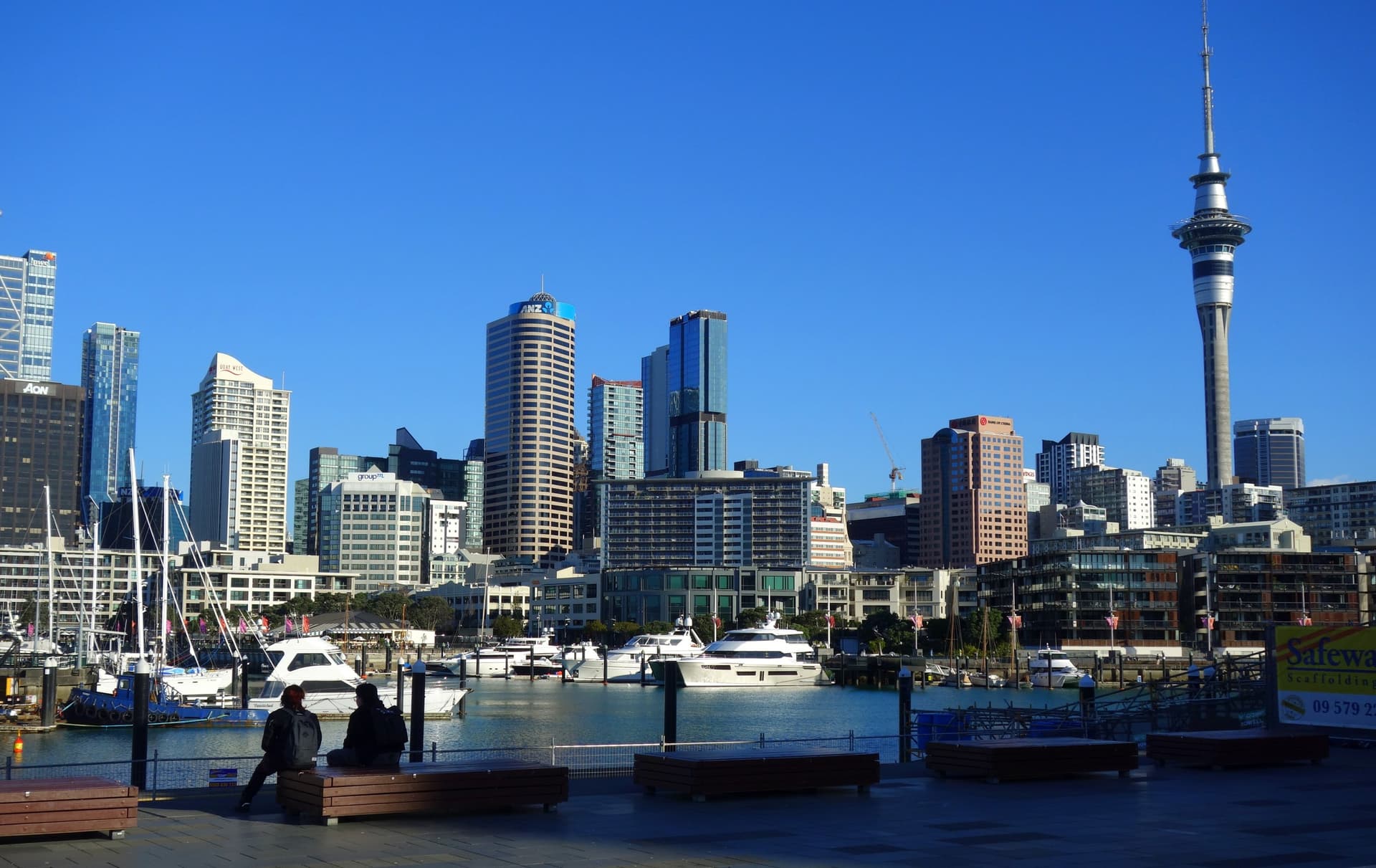 De jachthaven van de Viaduct Harbour in Auckland met hoge kantoortorens en de slanke Sky Tower onder een strakblauwe lucht
