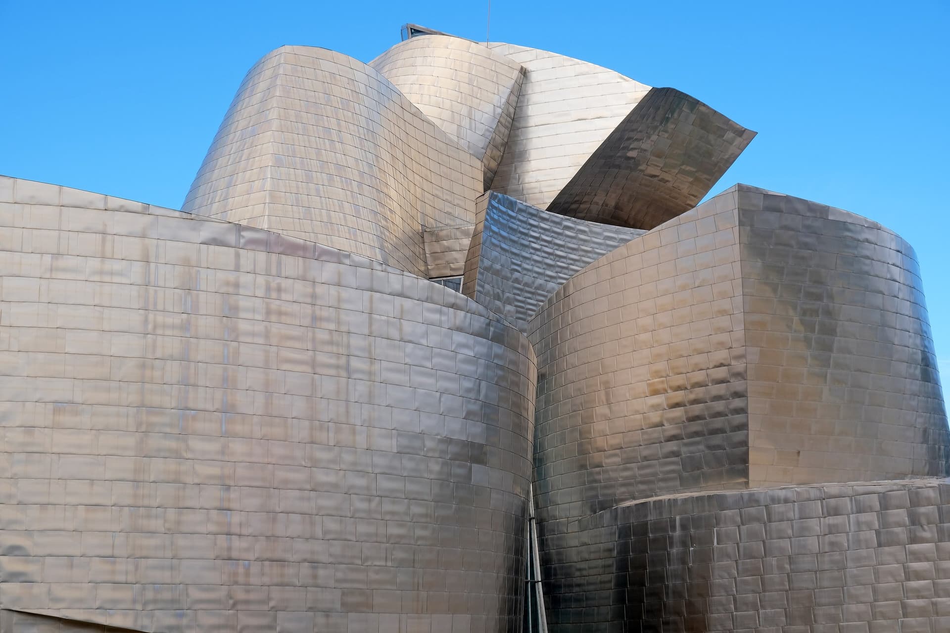 De glanzende titanium gevels van het Guggenheim Museum in Bilbao tegen een strakblauwe lucht