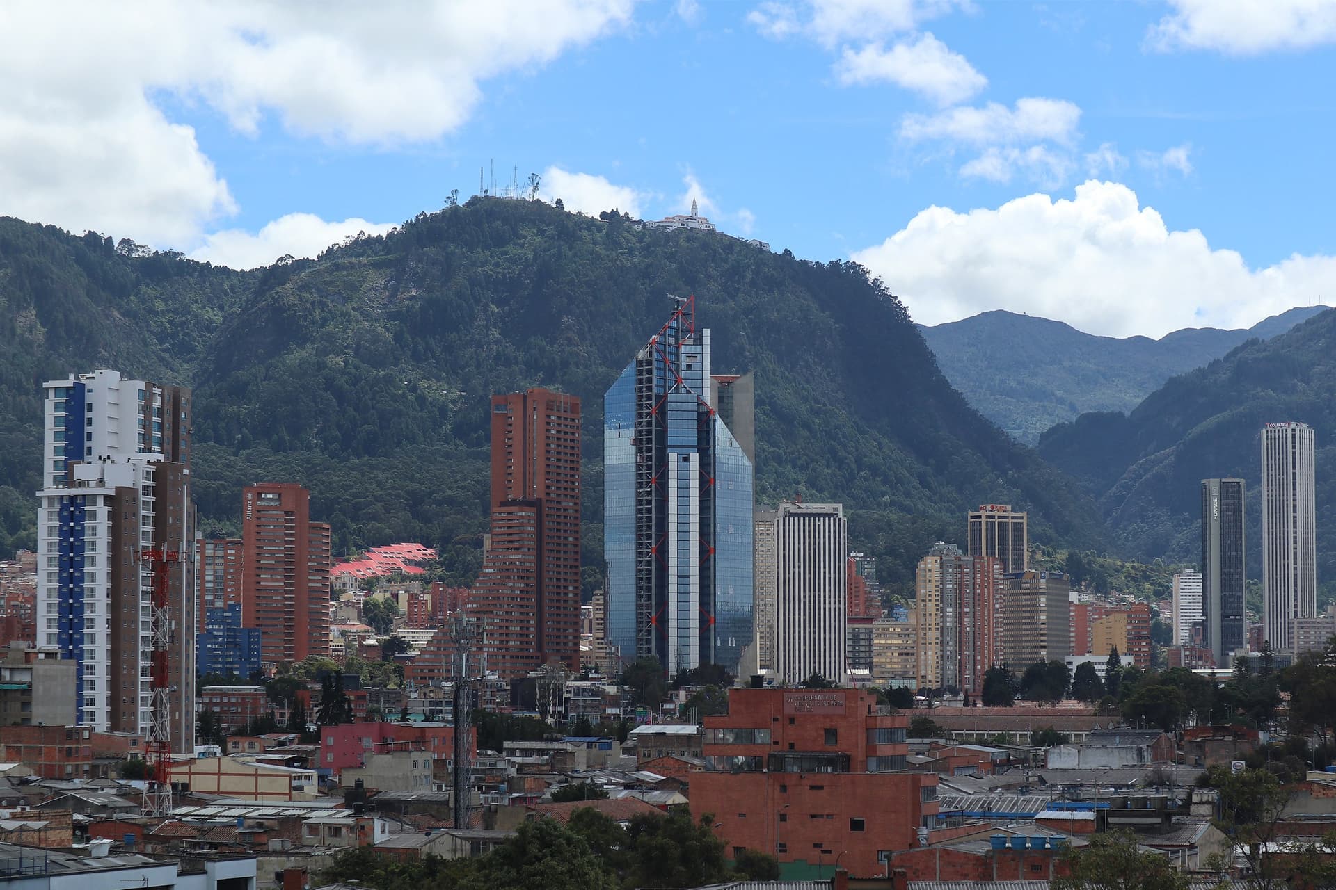 Hoge torens in het centrum van Bogotá tegen de groene bergwand van Monserrate, onder een blauwe lucht met stapelwolken