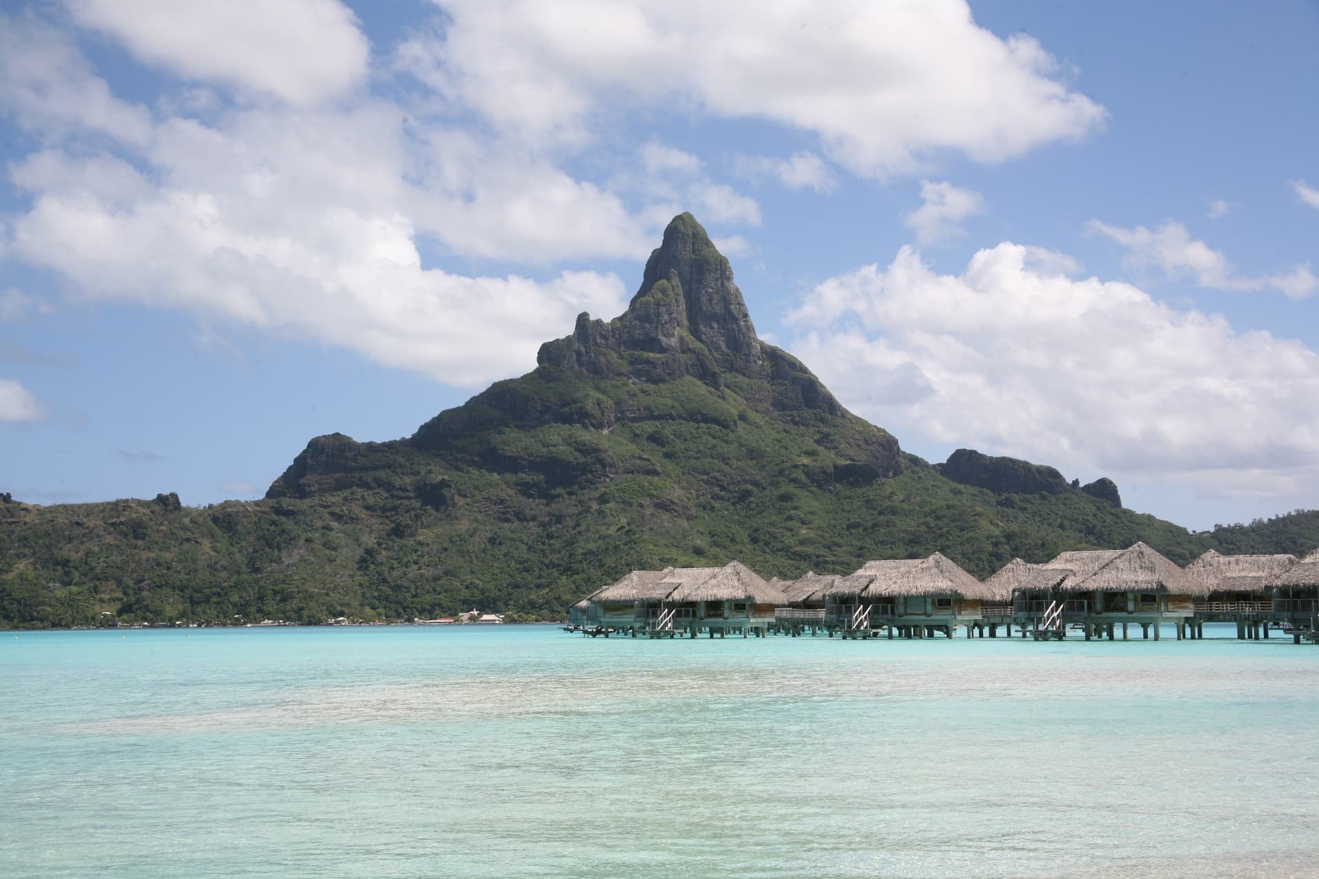 De piek van Mont Otemanu op Bora Bora boven een lichtblauwe lagune met een rij overwaterbungalows