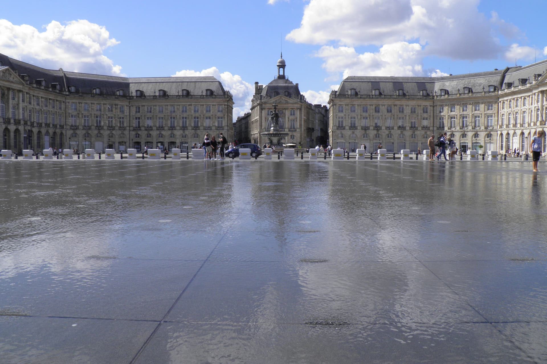 De Place de la Bourse in Bordeaux weerspiegeld in de Miroir d'eau onder een blauwe lucht met stapelwolken
