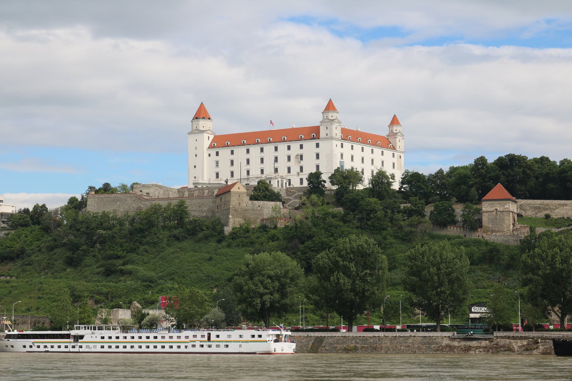 De witte burcht van Bratislava met vier torens op de heuvel boven de Donau, met een rivierschip op het water
