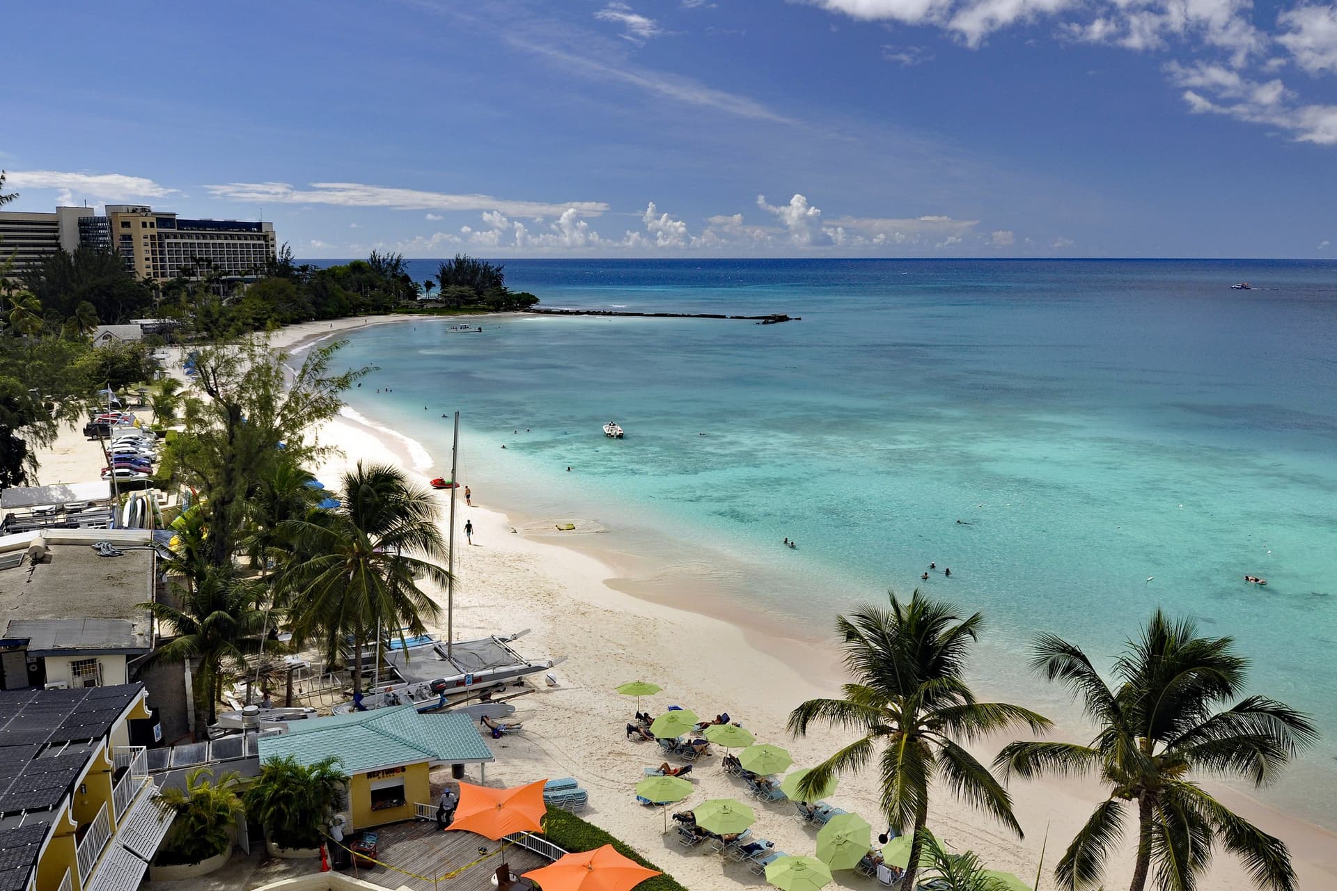 Het witte zandstrand van Carlisle Bay bij Bridgetown met palmbomen, parasols en helder turquoise water
