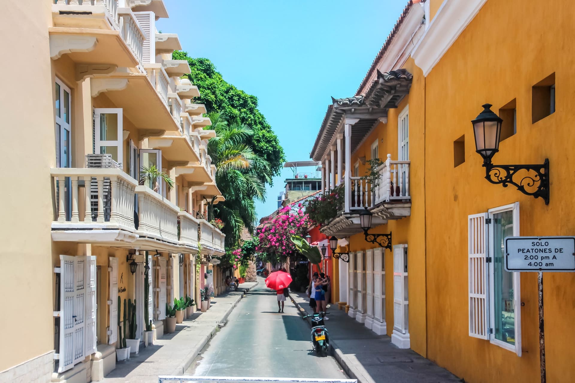 Een straatje in de ommuurde oude stad van Cartagena met gele en witte koloniale huizen, houten balkons en bloeiende bougainville