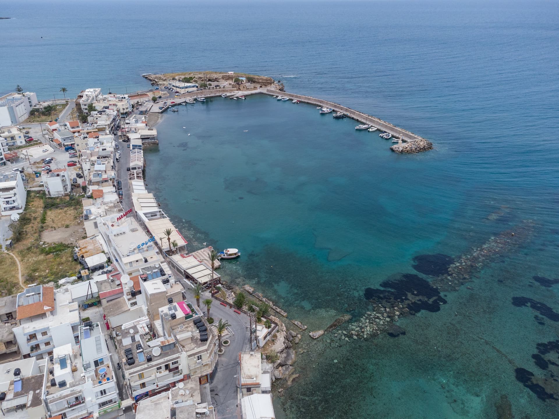 Luchtfoto van de haven van Chersonissos op Kreta, met witte huizen langs de kade en helder turquoise water rond de pier