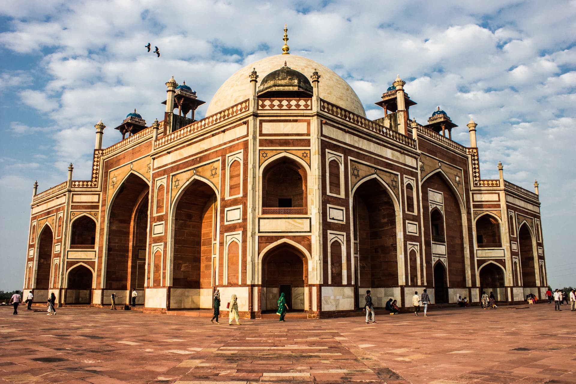 Het rood-witte mausoleum van Humayun in Delhi met zijn marmeren koepel en hoge bogen, op een zonnige dag met bezoekers op het plein