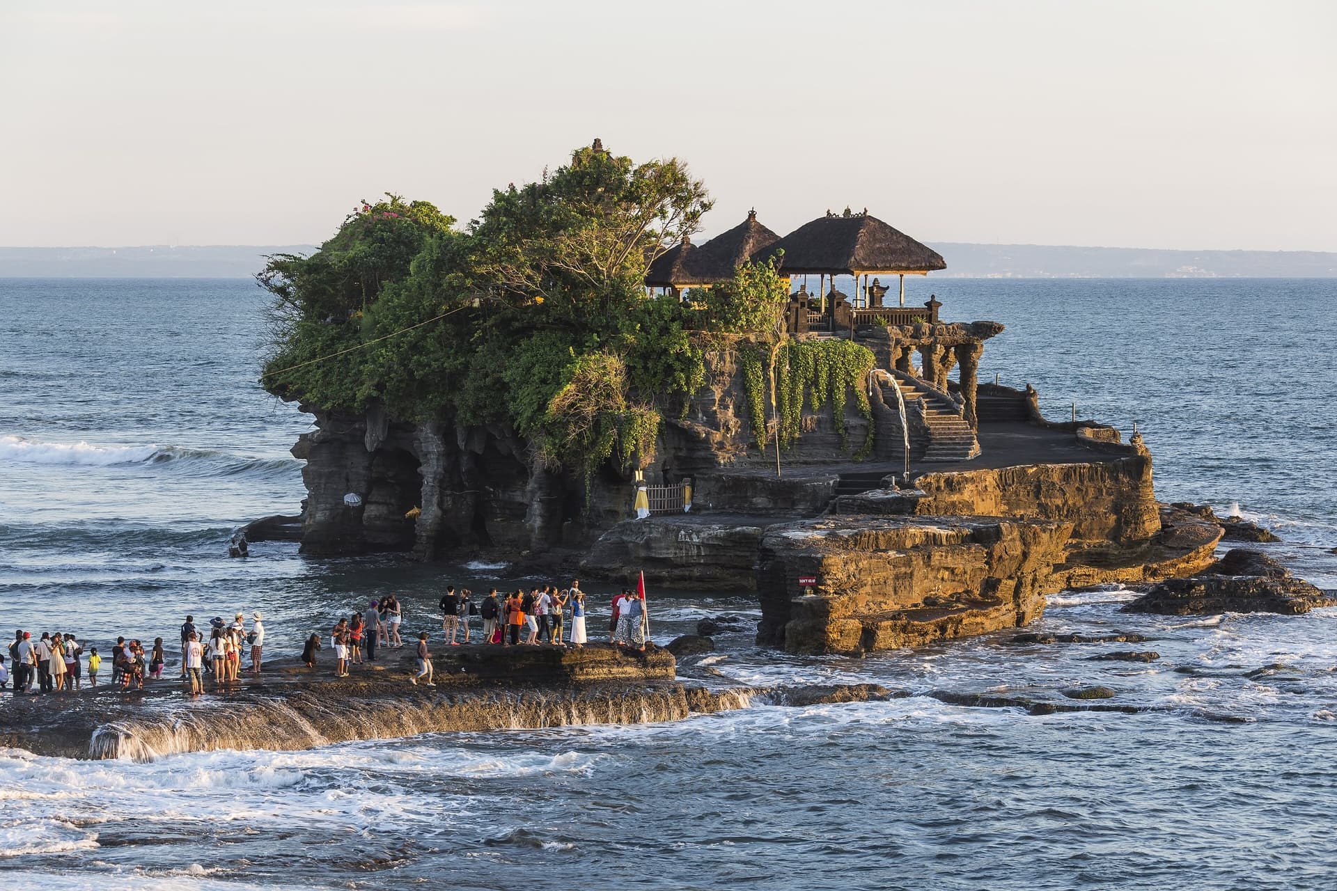 Zeetempel Pura Tanah Lot op een rots in de branding voor de kust van Bali, in het warme licht van de late middag, met bezoekers op de rotsen bij eb
