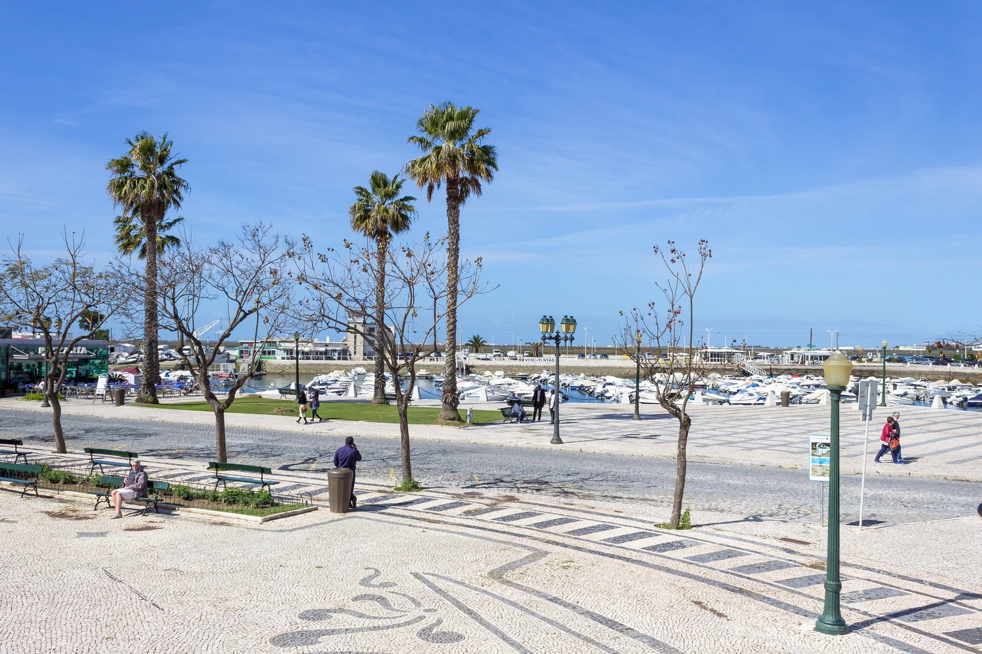 Palmbomen en een plein met Portugees mozaïek bij de jachthaven van Faro onder een blauwe lucht