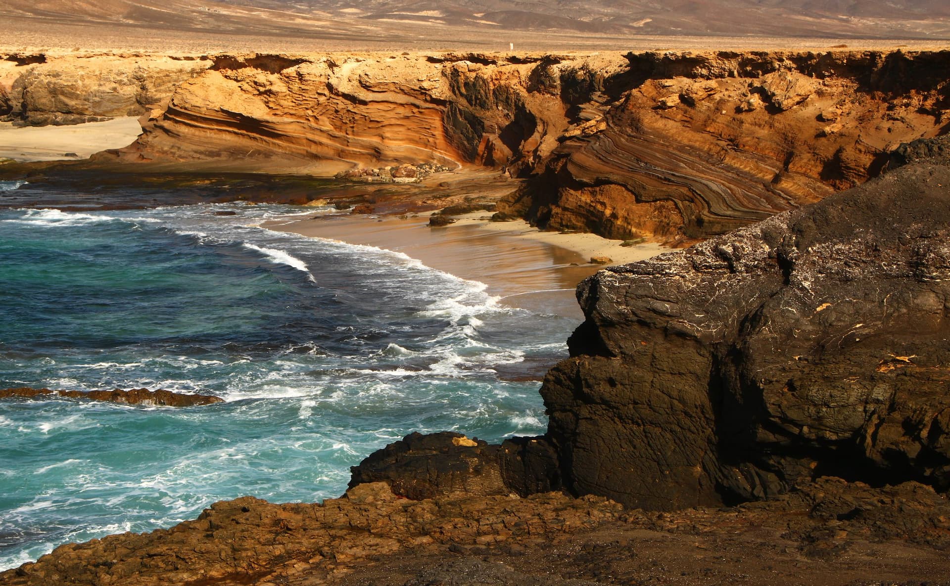 Gelaagde okerkleurige kliffen en woeste golven bij de Playa de Ojos in het zuiden van Fuerteventura