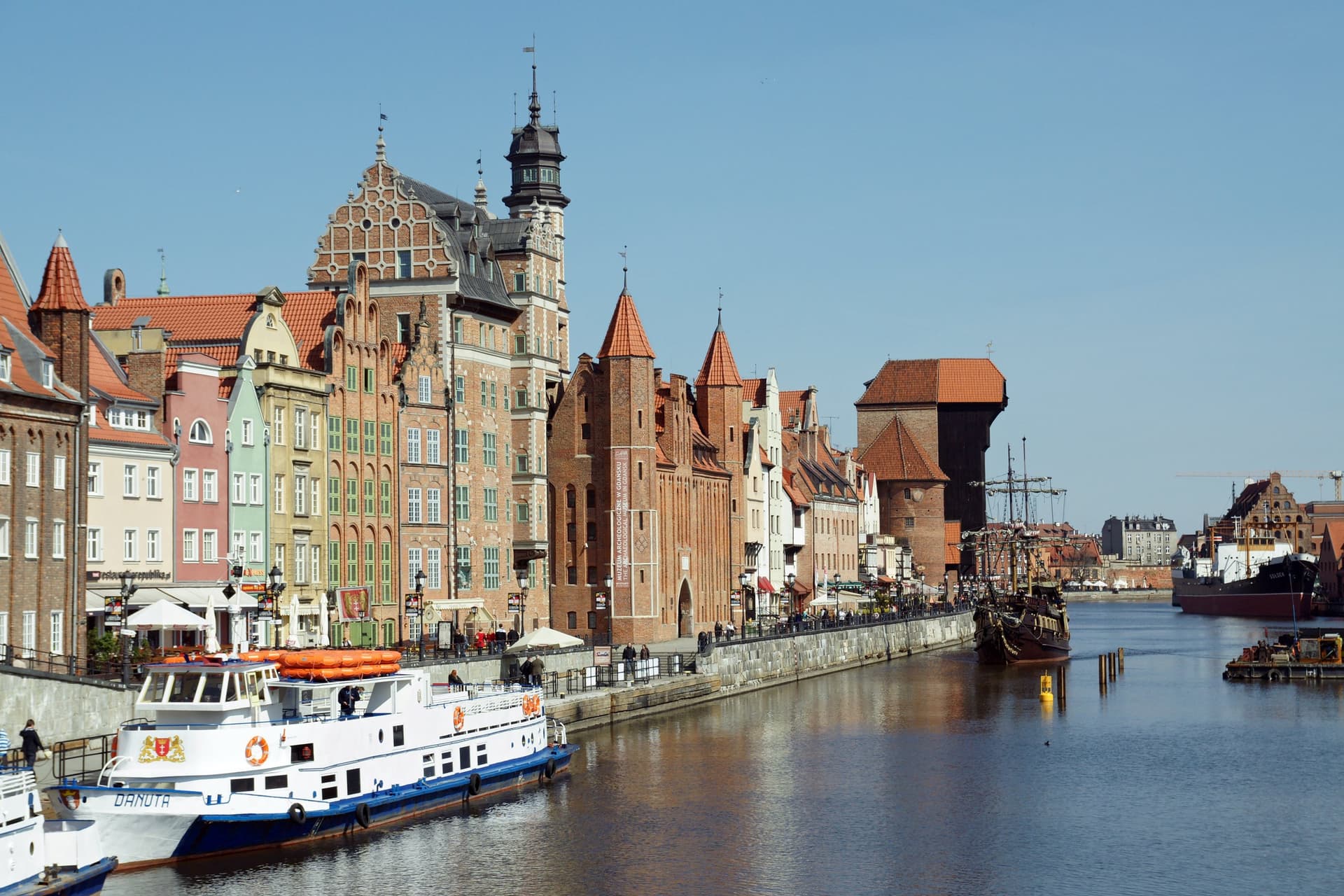 Gevels aan de Motława in Gdańsk met de middeleeuwse houten kraan en rondvaartboten op een zonnige dag