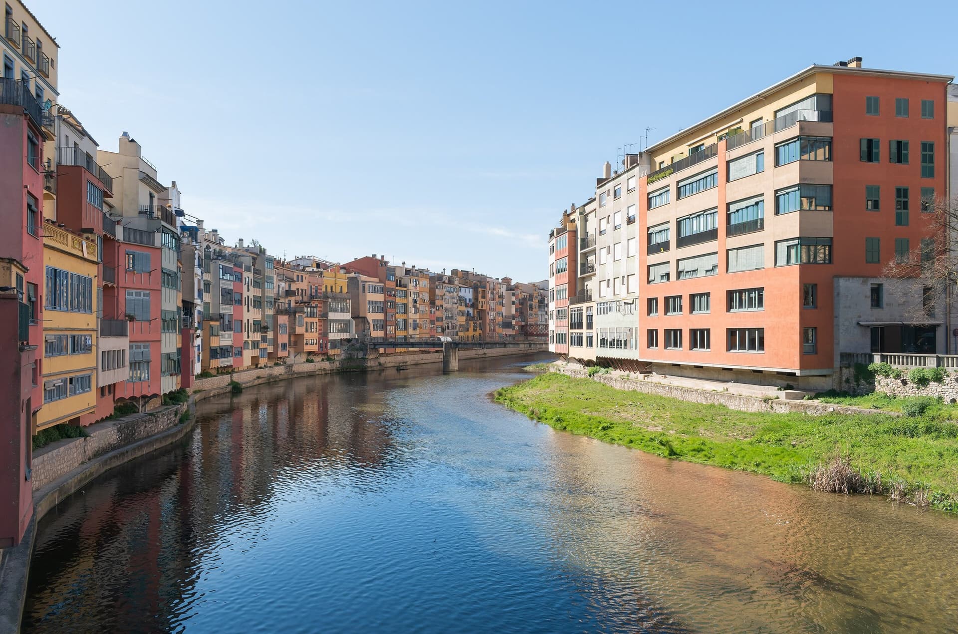 Kleurige huizen aan de rivier de Onyar in Girona, weerspiegeld in het water onder een blauwe lucht