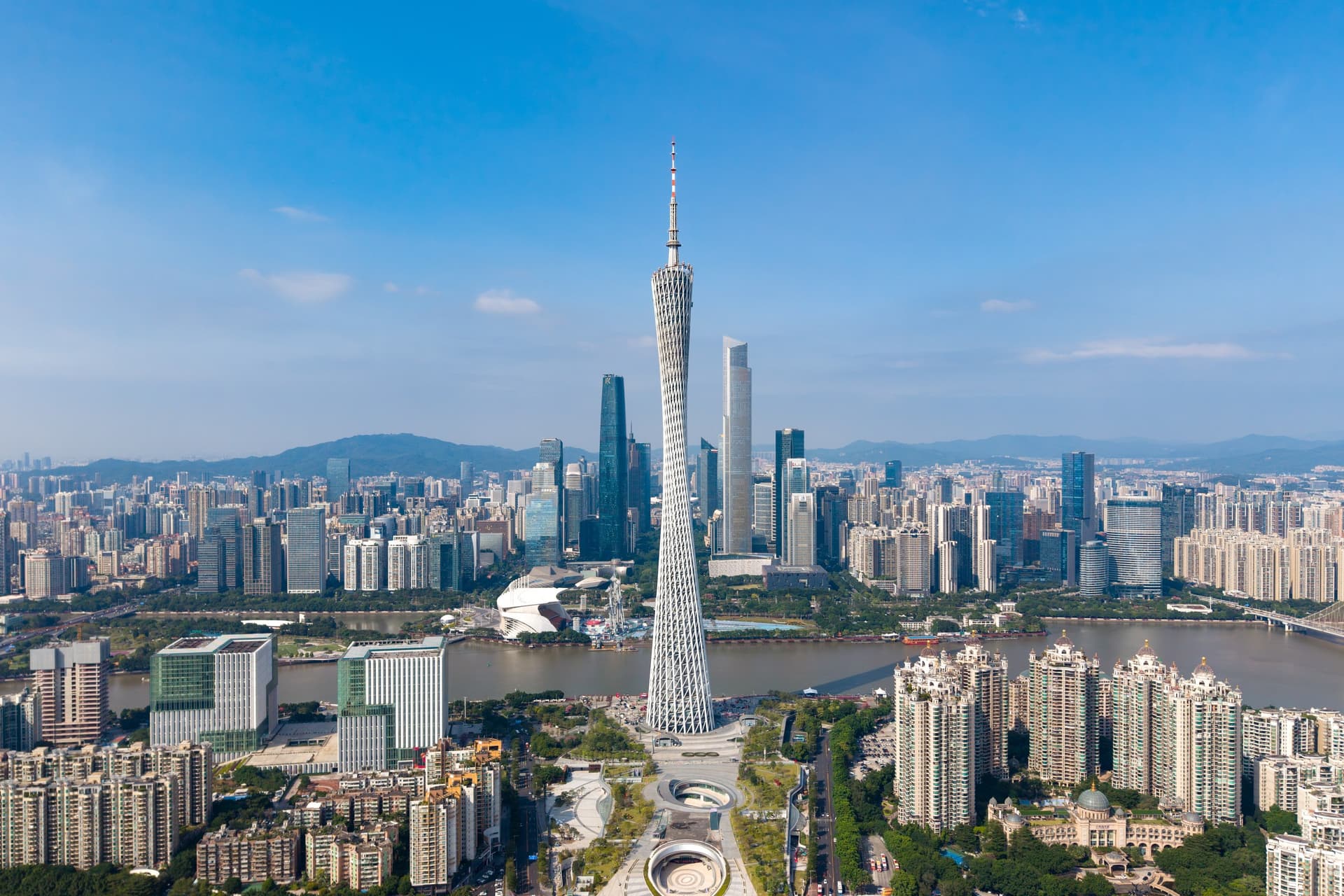 Luchtfoto van de slanke Canton Tower in Guangzhou aan de Parelrivier, met de wolkenkrabbers van Zhujiang New Town erachter onder een blauwe lucht
