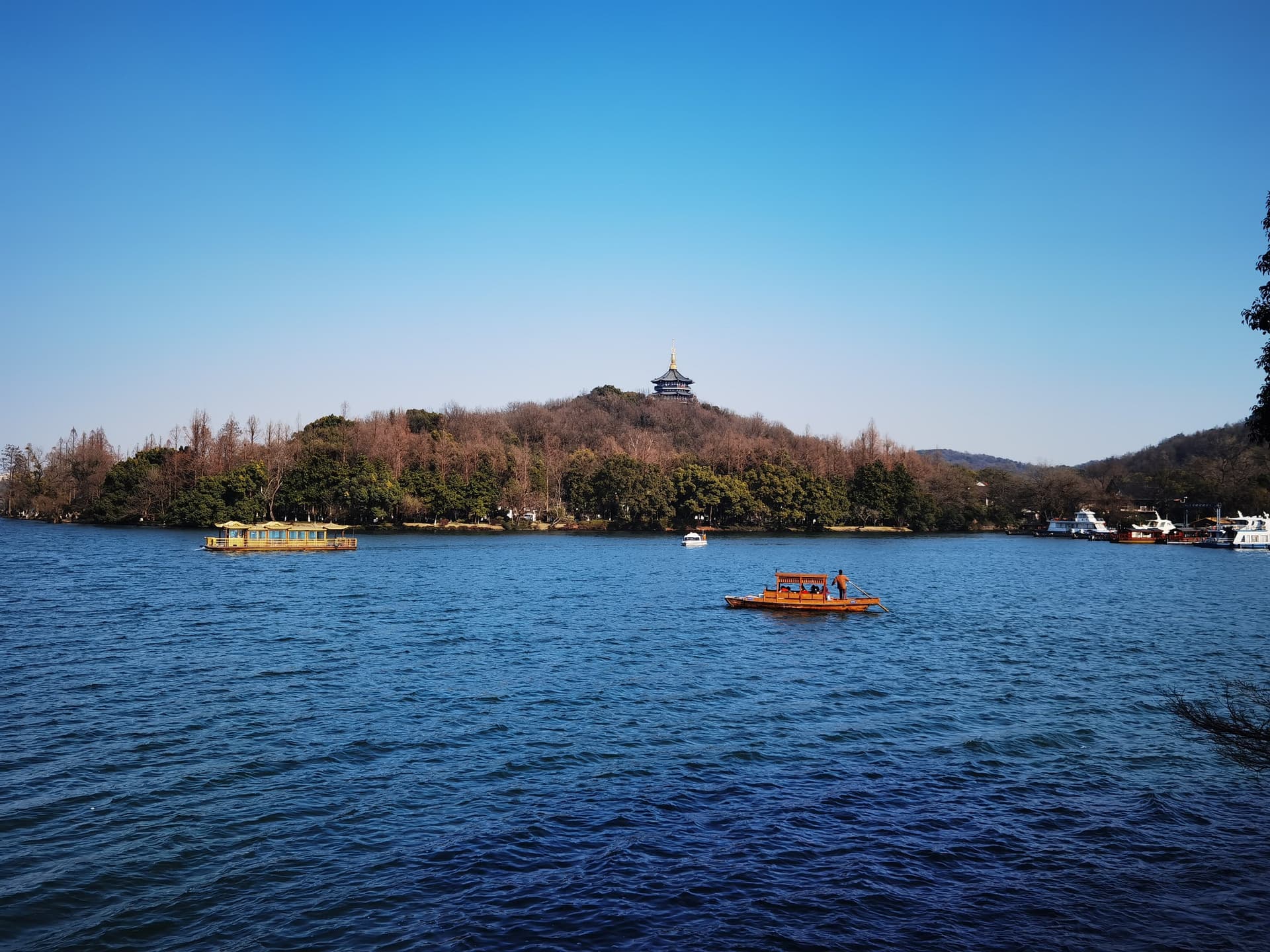 Het blauwe water van het Westmeer in Hangzhou met rondvaartbootjes en de Leifeng-pagode op een beboste heuvel aan de overkant