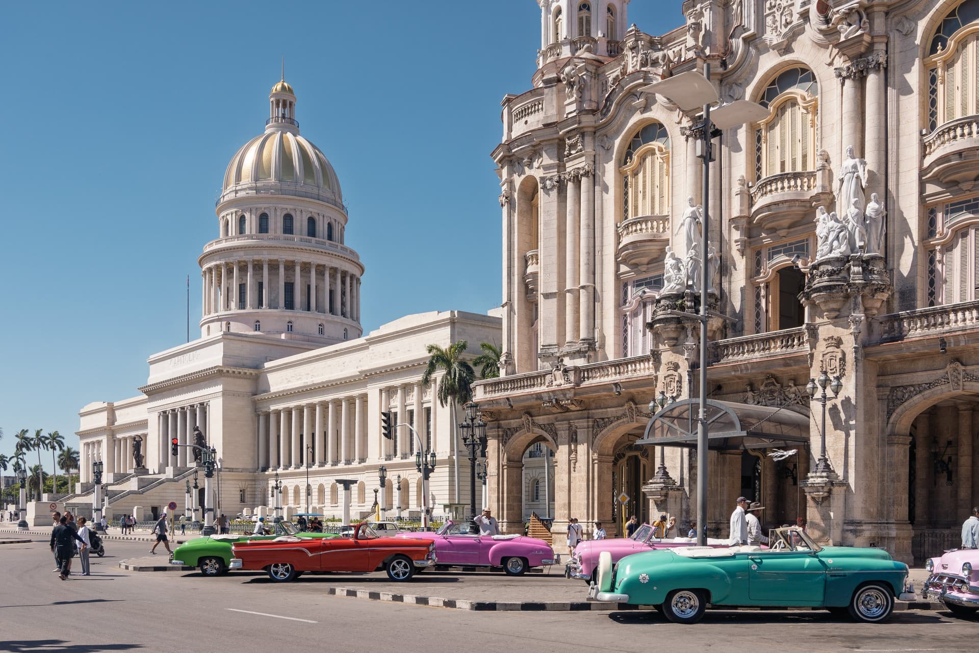 Het Capitolio met zijn witte koepel en het barokke Gran Teatro in Havana, met kleurrijke Amerikaanse oldtimers langs de straat onder een blauwe lucht