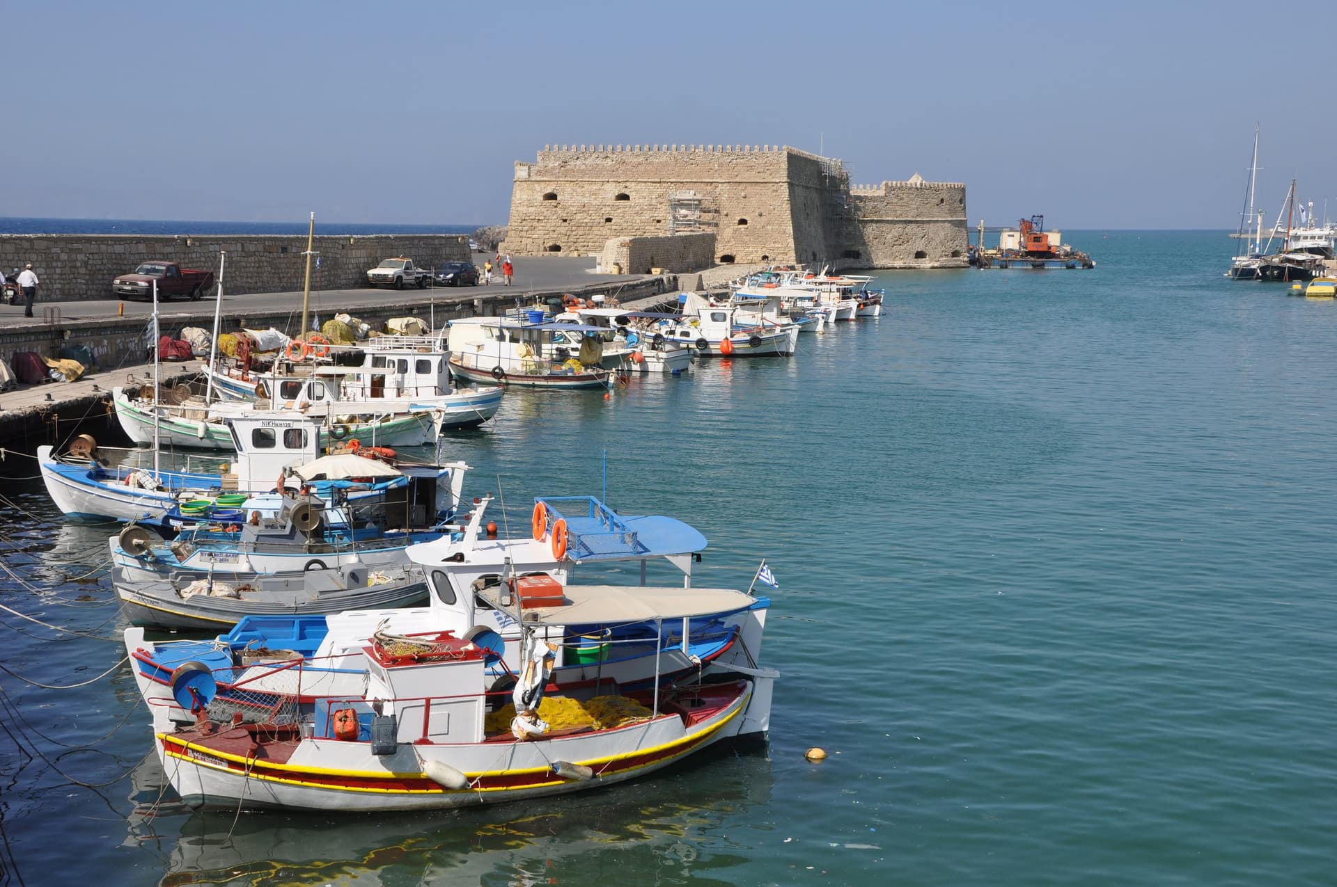 Kleurrijke vissersbootjes in de oude haven van Heraklion met het Venetiaanse fort Koules op de achtergrond