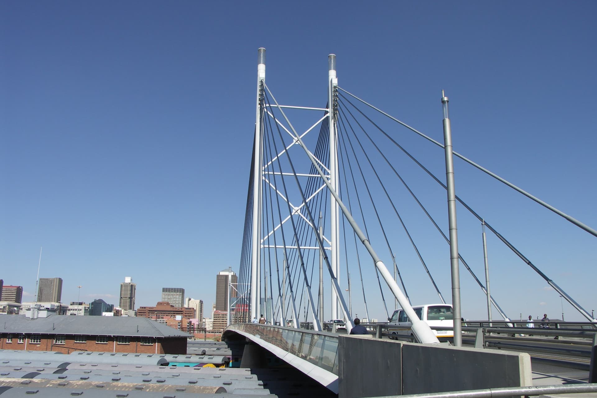 De witte pylonen en tuikabels van de Nelson Mandelabrug in Johannesburg tegen een strakblauwe lucht, met de torens van het centrum op de achtergrond