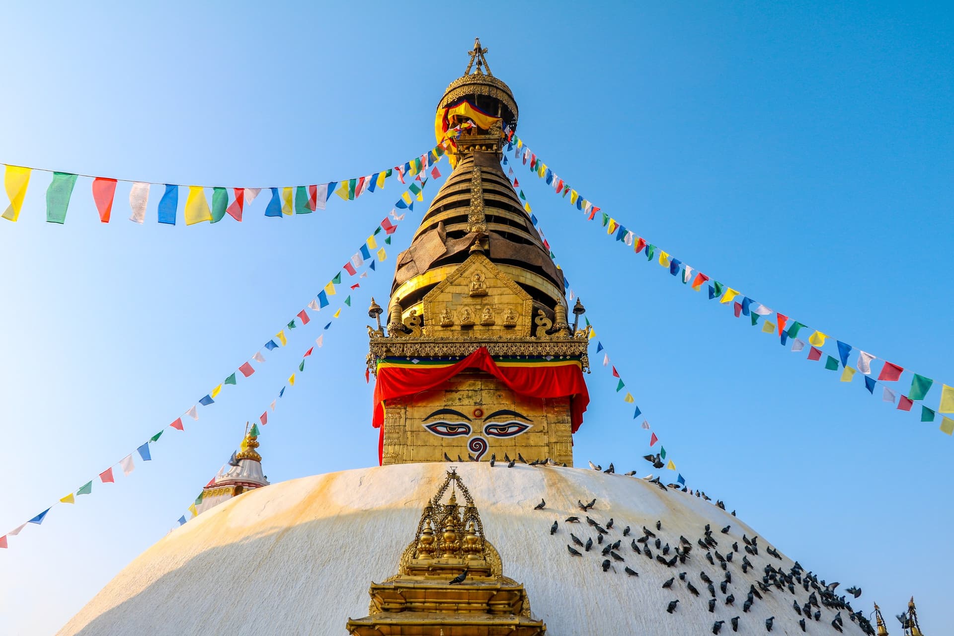 De vergulde spits van de stoepa van Swayambhunath in Kathmandu met de geschilderde ogen van Boeddha en kleurige gebedsvlaggen tegen een blauwe lucht