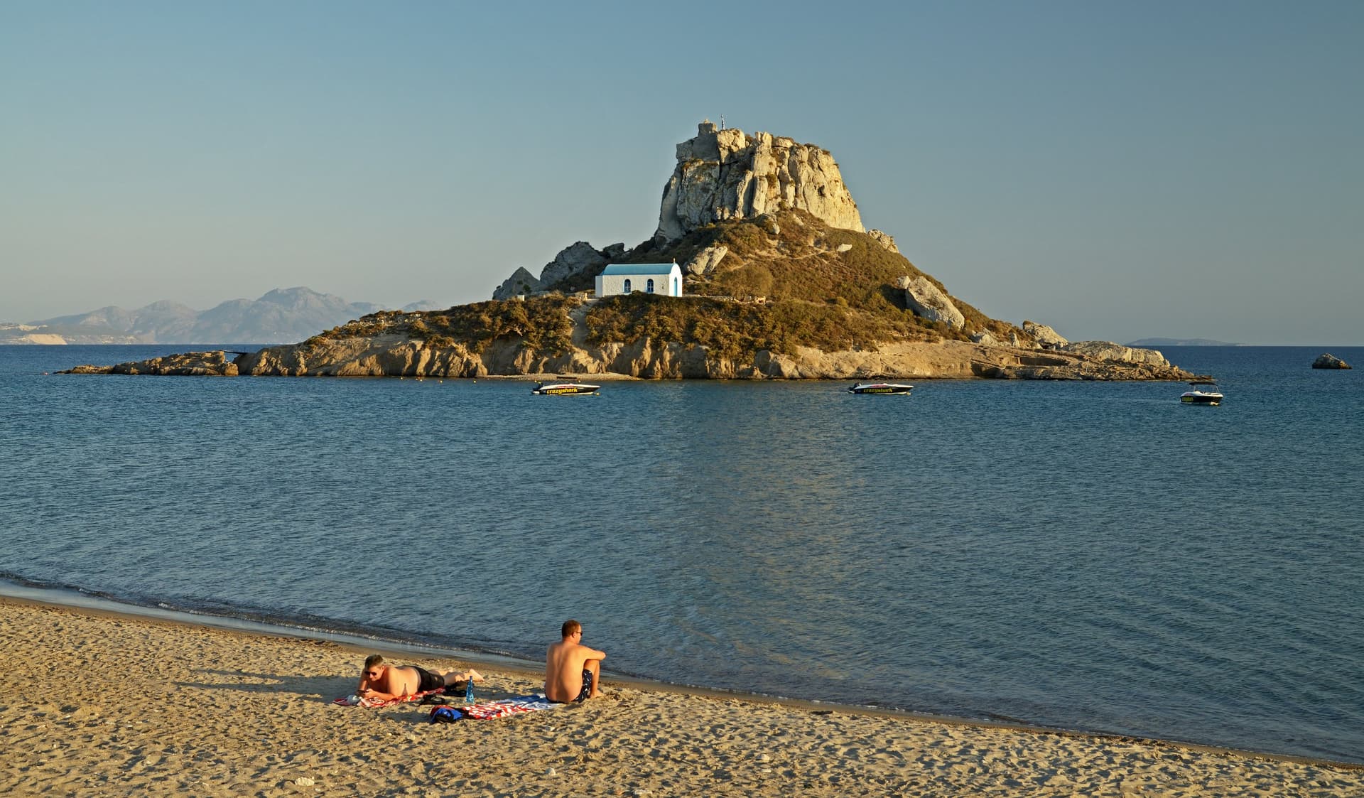 Het eilandje Kastri met de kapel van Sint-Nicolaas voor het strand van Kefalos op Kos, in warm avondlicht