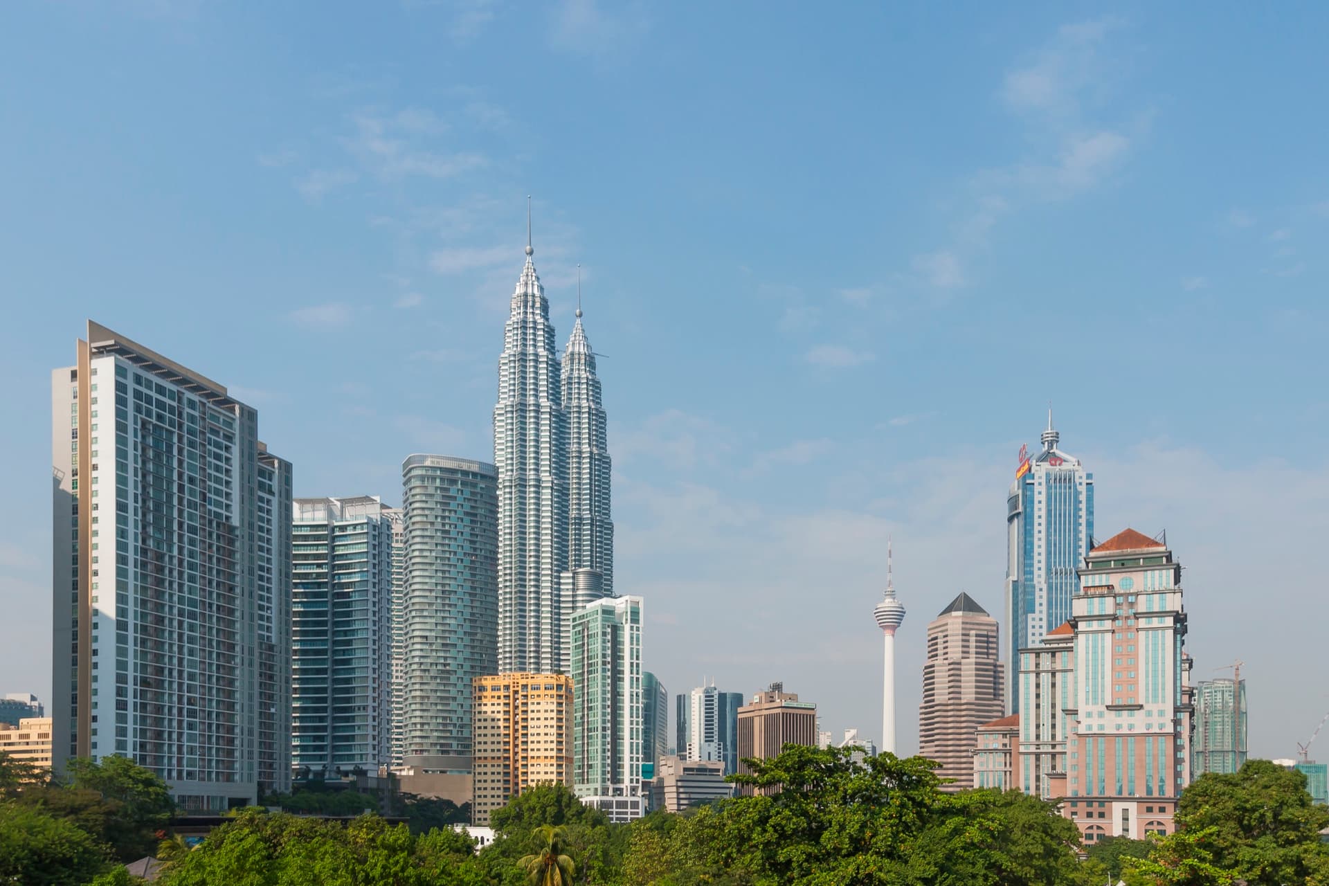 Skyline van Kuala Lumpur onder een blauwe lucht, met de Petronas Twin Towers, de KL Tower en torens rond het KLCC boven het groen