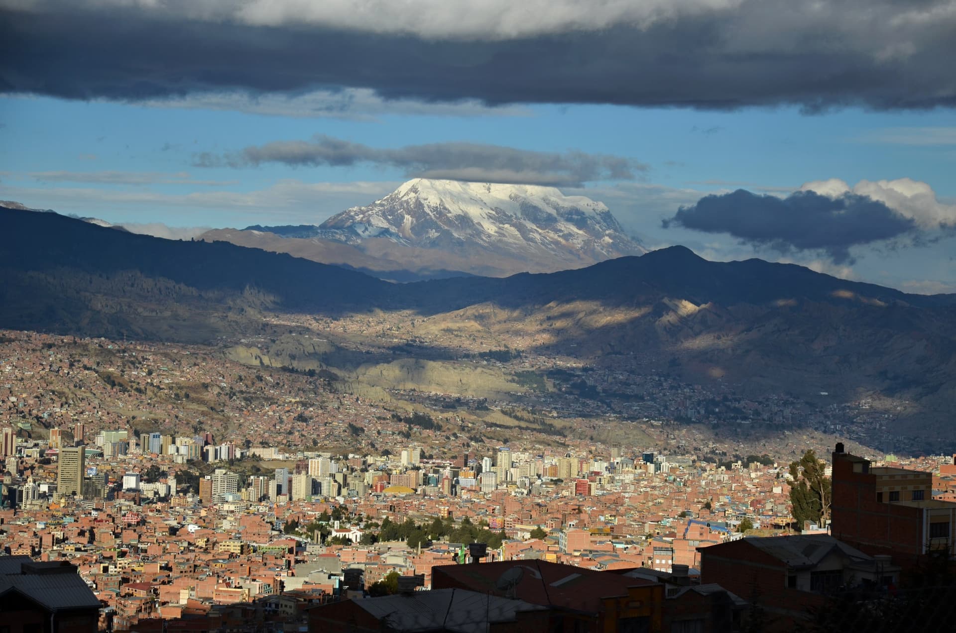 La Paz ligt uitgestrekt in een dal, met achter de stad de besneeuwde toppen van de Illimani onder donkere wolken