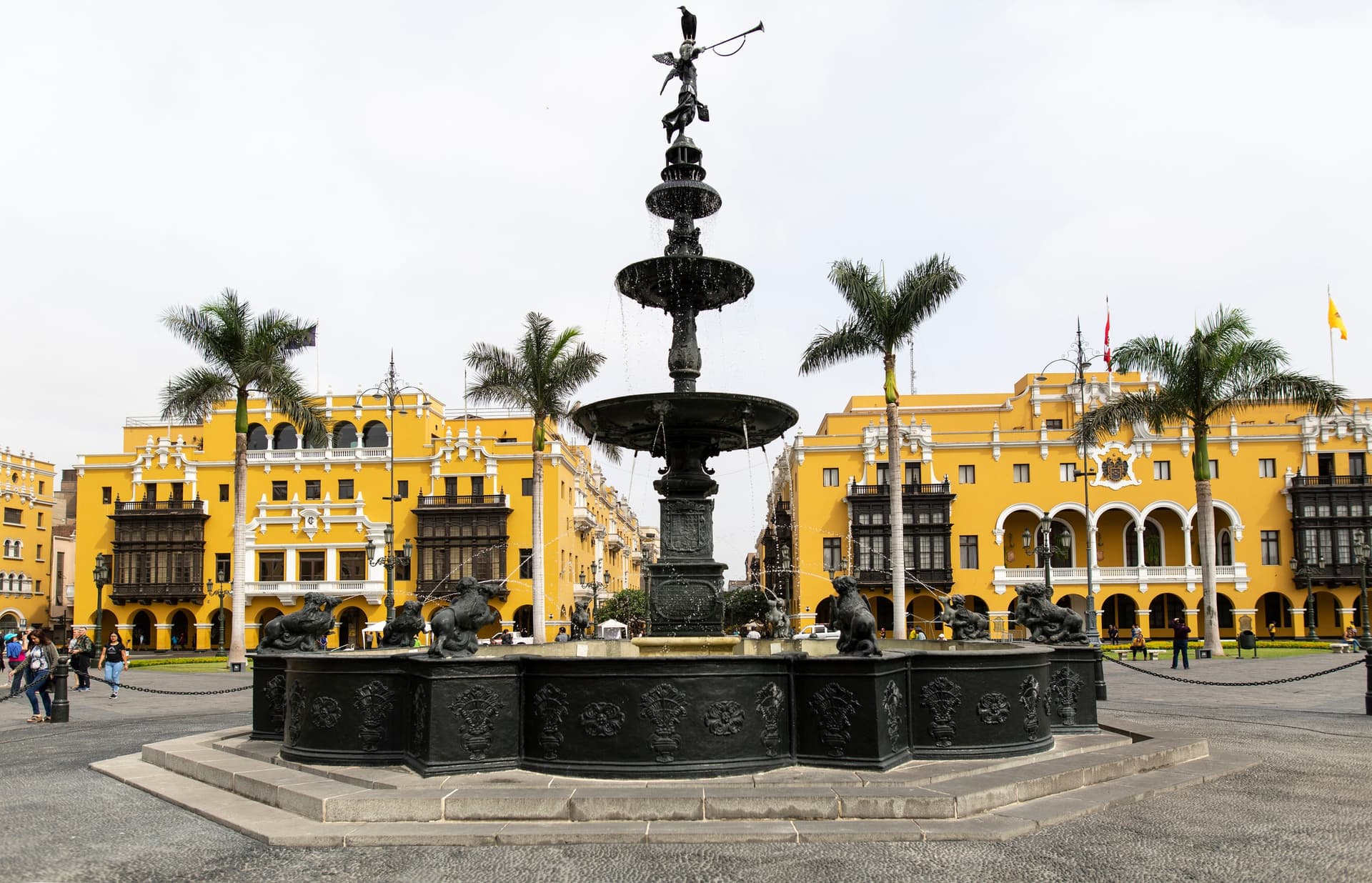 De bronzen fontein op de Plaza Mayor van Lima met palmen en gele koloniale gebouwen met houten balkons op de achtergrond