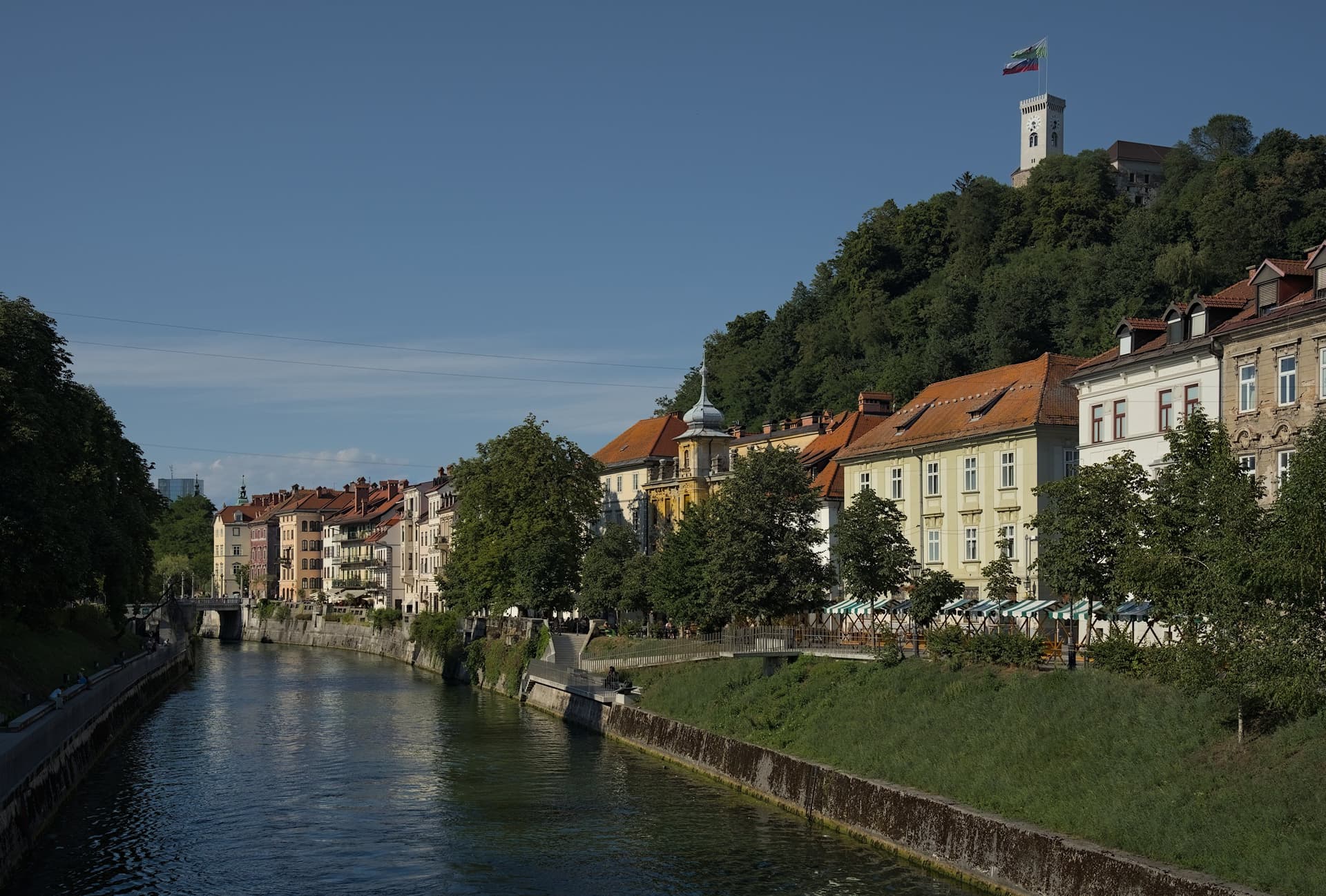 De rivier de Ljubljanica in Ljubljana met gevels aan de kade en de burcht op de beboste heuvel