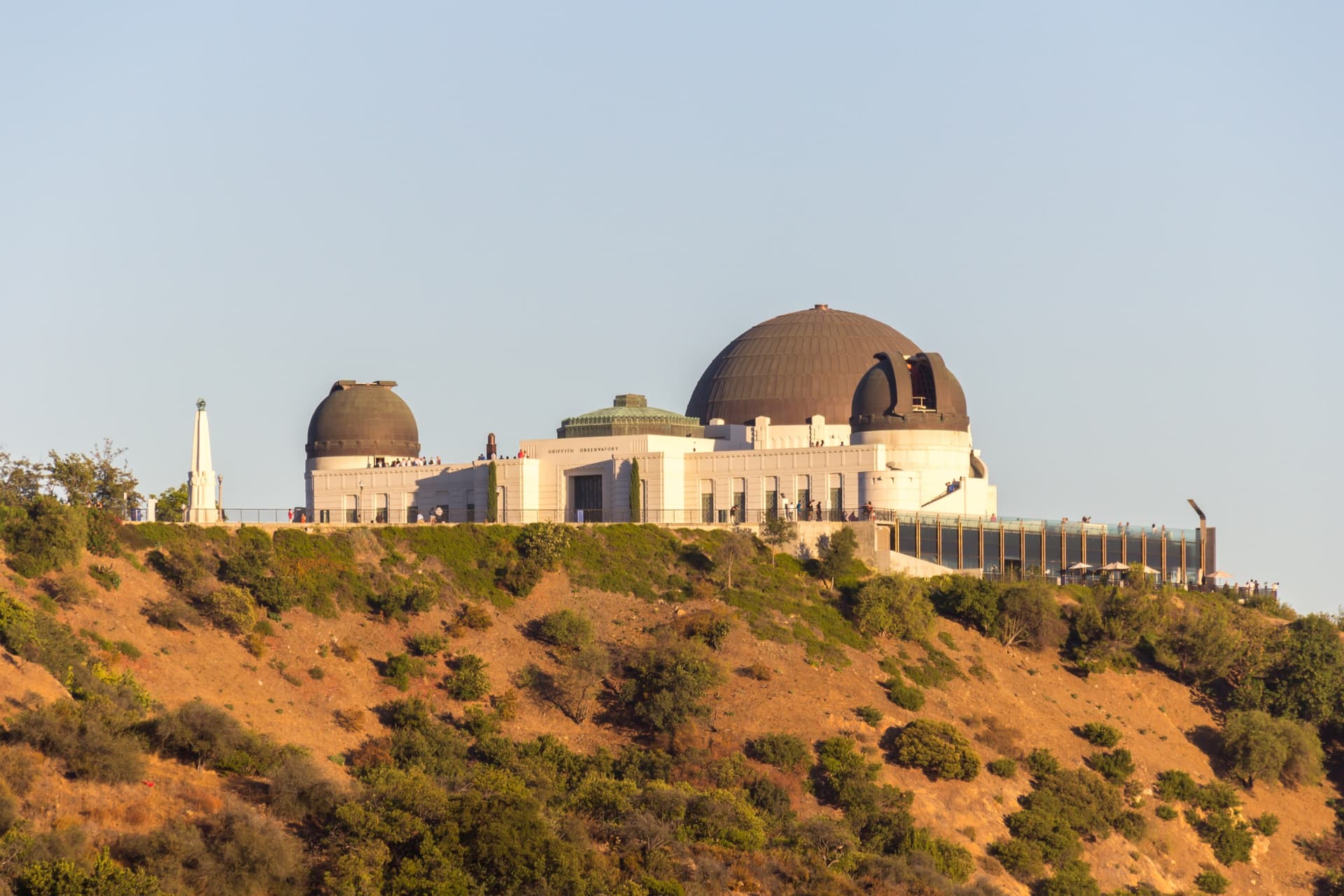 De witte Griffith Observatory met koperen koepels op een droge, begroeide heuvel in Los Angeles onder een strakblauwe lucht