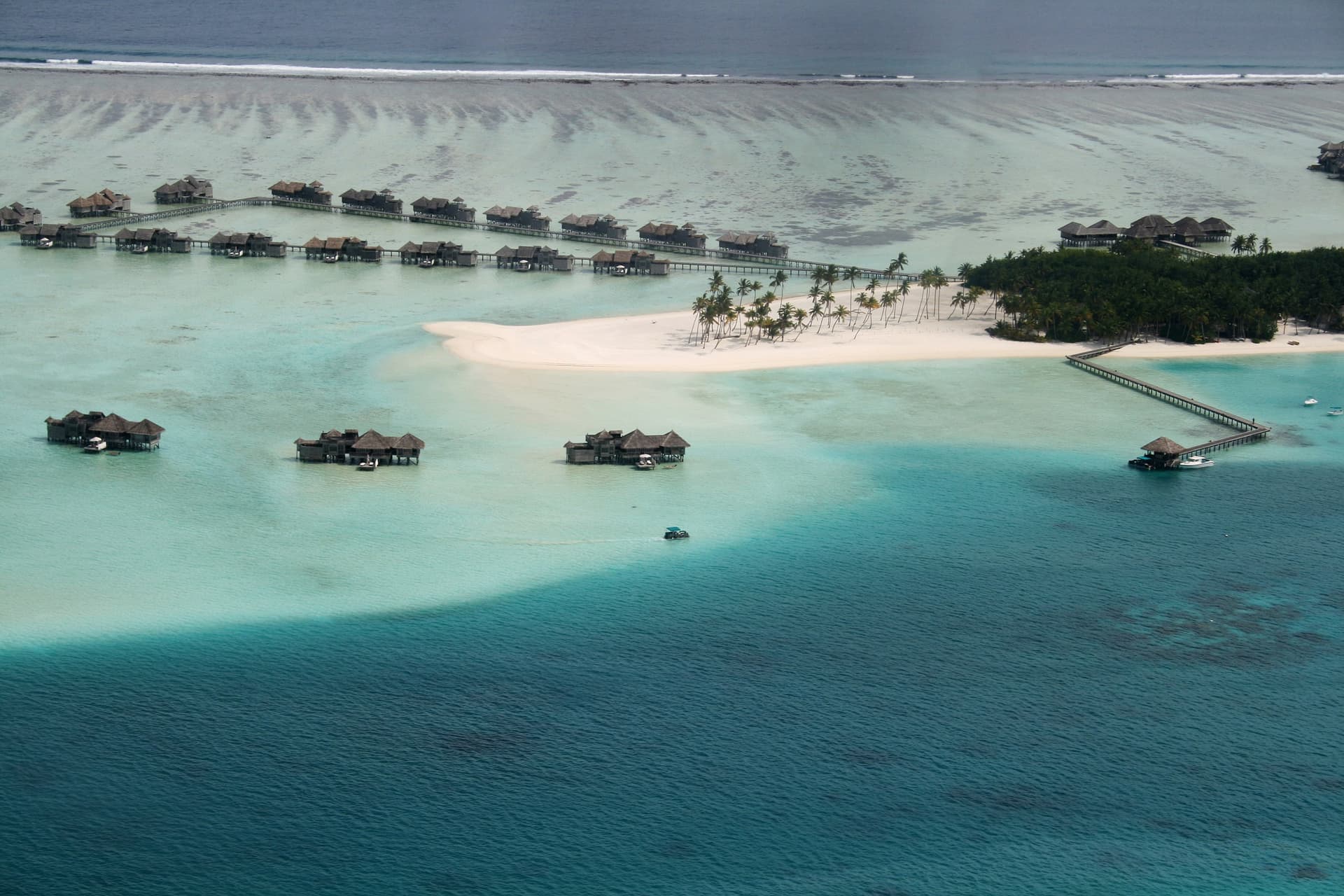 Luchtfoto van een Maldivisch resorteiland met watervilla's op palen, een witte zandbank met palmen en turquoise lagunes in de Indische Oceaan