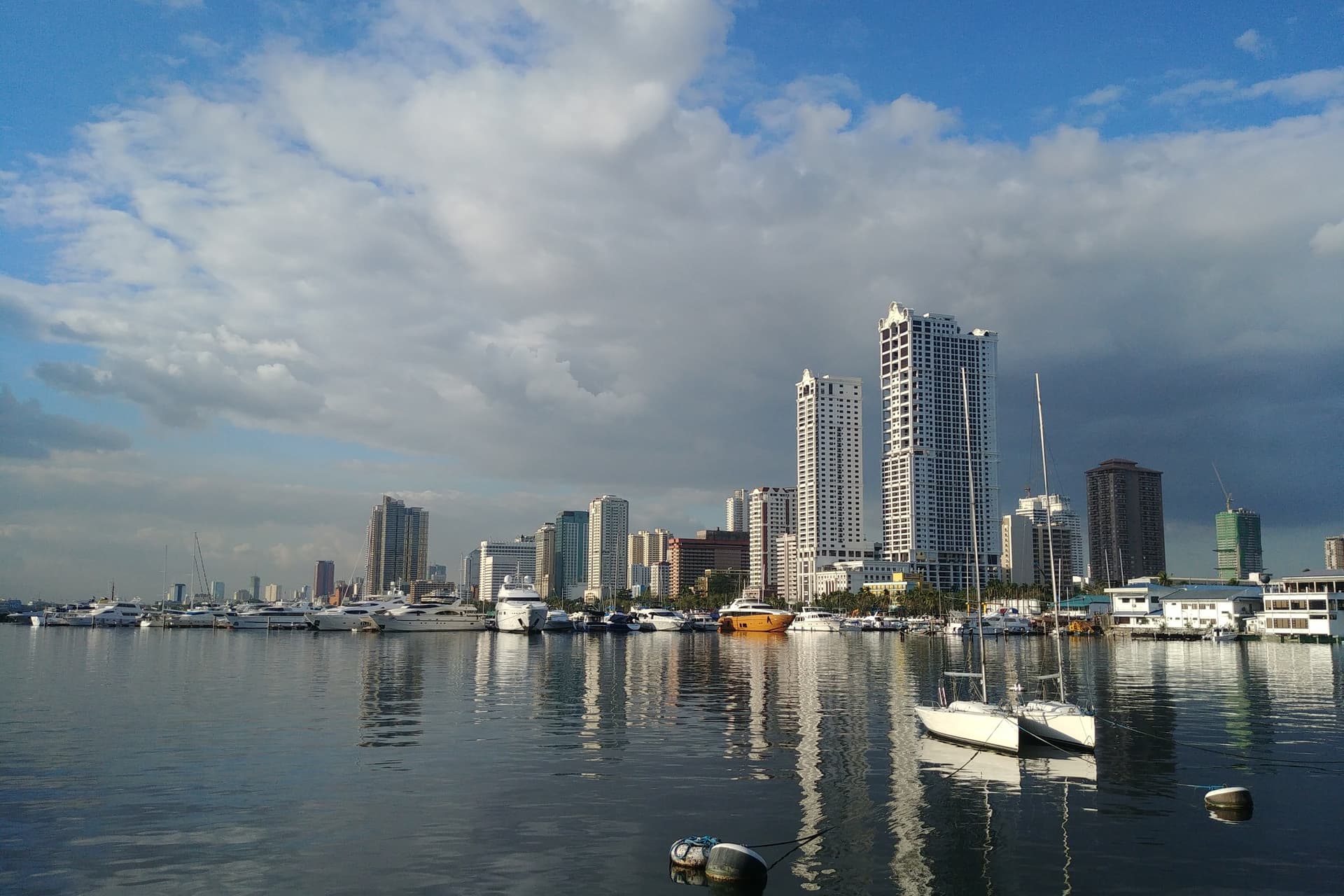 Zeilboten in de haven aan de Baai van Manila met de hoge torens van de stad erachter, weerspiegeld in het kalme water