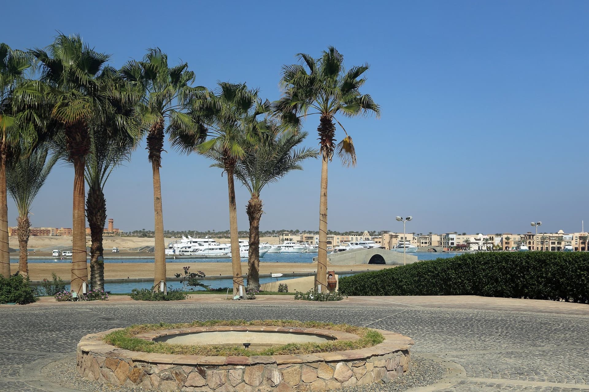 Palmbomen en een rotonde aan de jachthaven van Port Ghalib bij Marsa Alam, met jachten en lage gebouwen onder een blauwe lucht