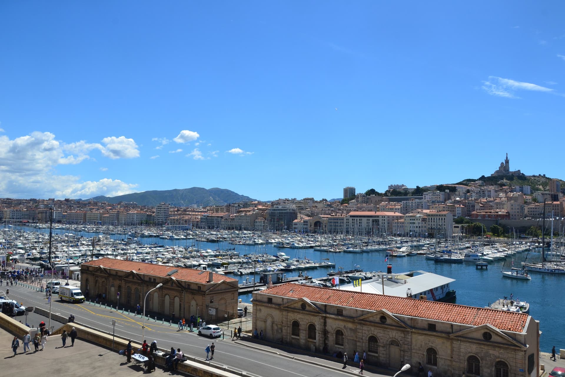 De Vieux-Port van Marseille vol zeilboten onder een blauwe lucht, met op de heuvel de basiliek Notre-Dame de la Garde