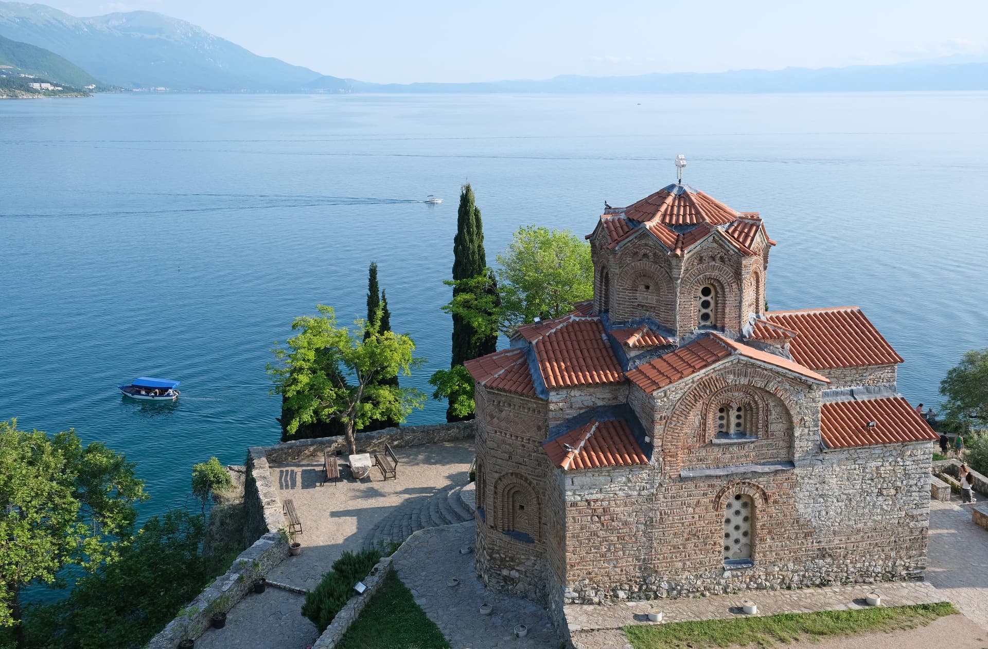 De kerk van Sint-Jan in Kaneo op een rots boven het Meer van Ohrid, met cipressen en bergen aan de overkant