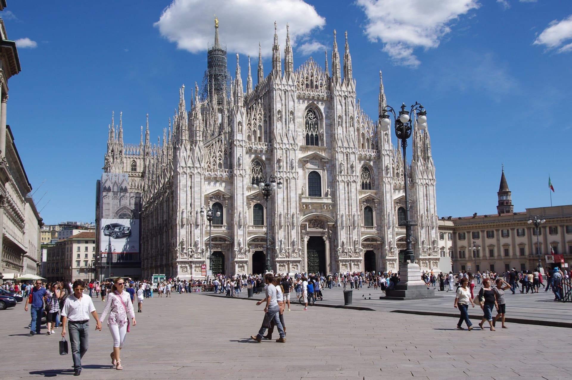 De witte marmeren gevel van de Dom van Milaan aan het Piazza del Duomo onder een blauwe lucht met wolken