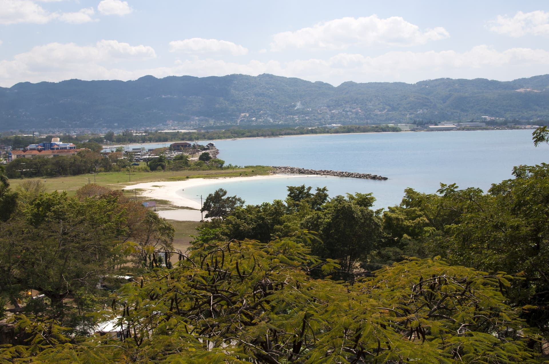 Uitzicht over de oostkant van Montego Bay: een lichte zandbaai en turquoise water tegen de groene heuvels van Jamaica