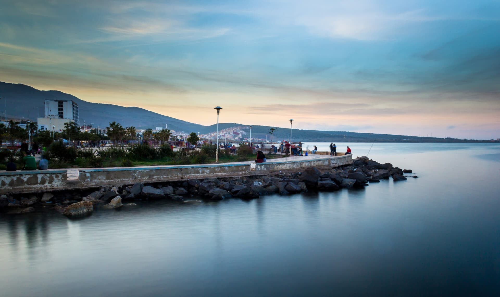 De boulevard van Nador aan de lagune Mar Chica bij zonsondergang, met wandelaars op de pier en bergen aan de horizon