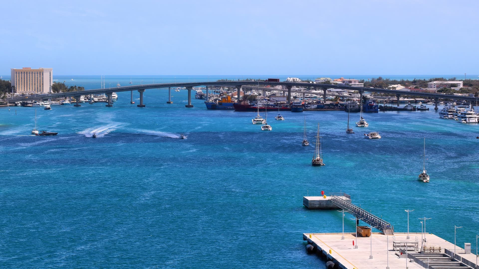 De turquoise haven van Nassau met zeilboten en een pier op de voorgrond en de brug naar Paradise Island op de achtergrond