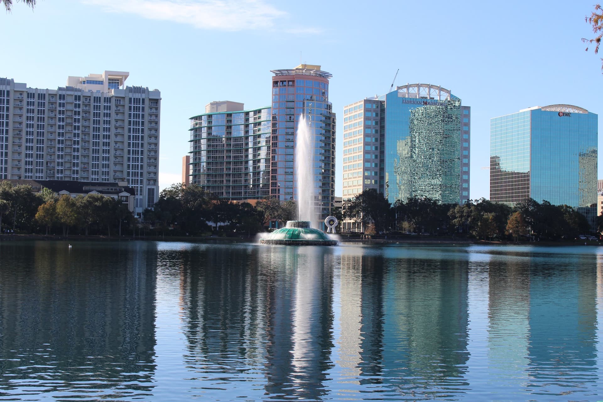 De fontein in Lake Eola met de glazen torens van Downtown Orlando die weerspiegelen in het water onder een blauwe lucht