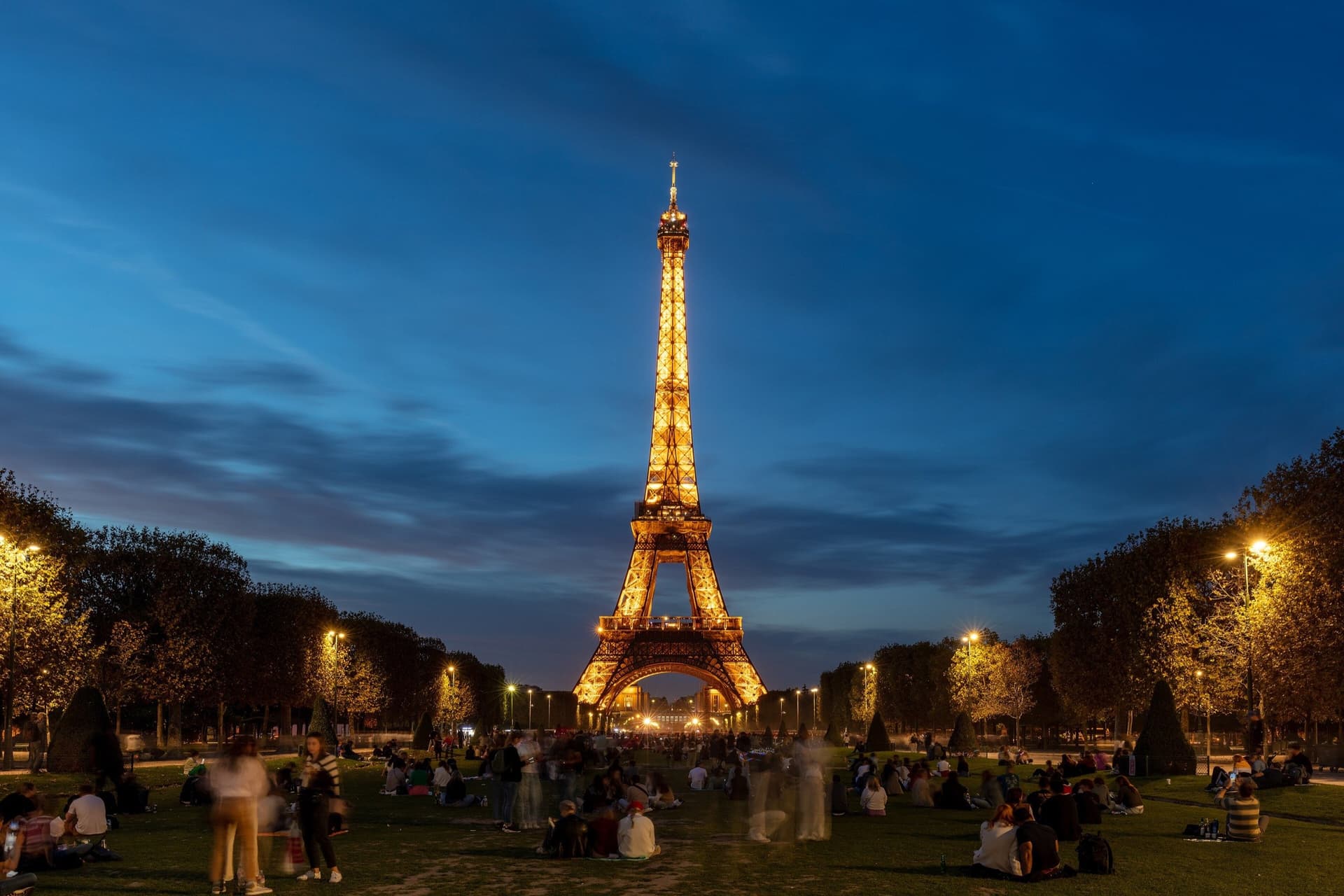 De verlichte Eiffeltoren in Parijs tijdens het blauwe uur, gezien vanaf het Champ de Mars