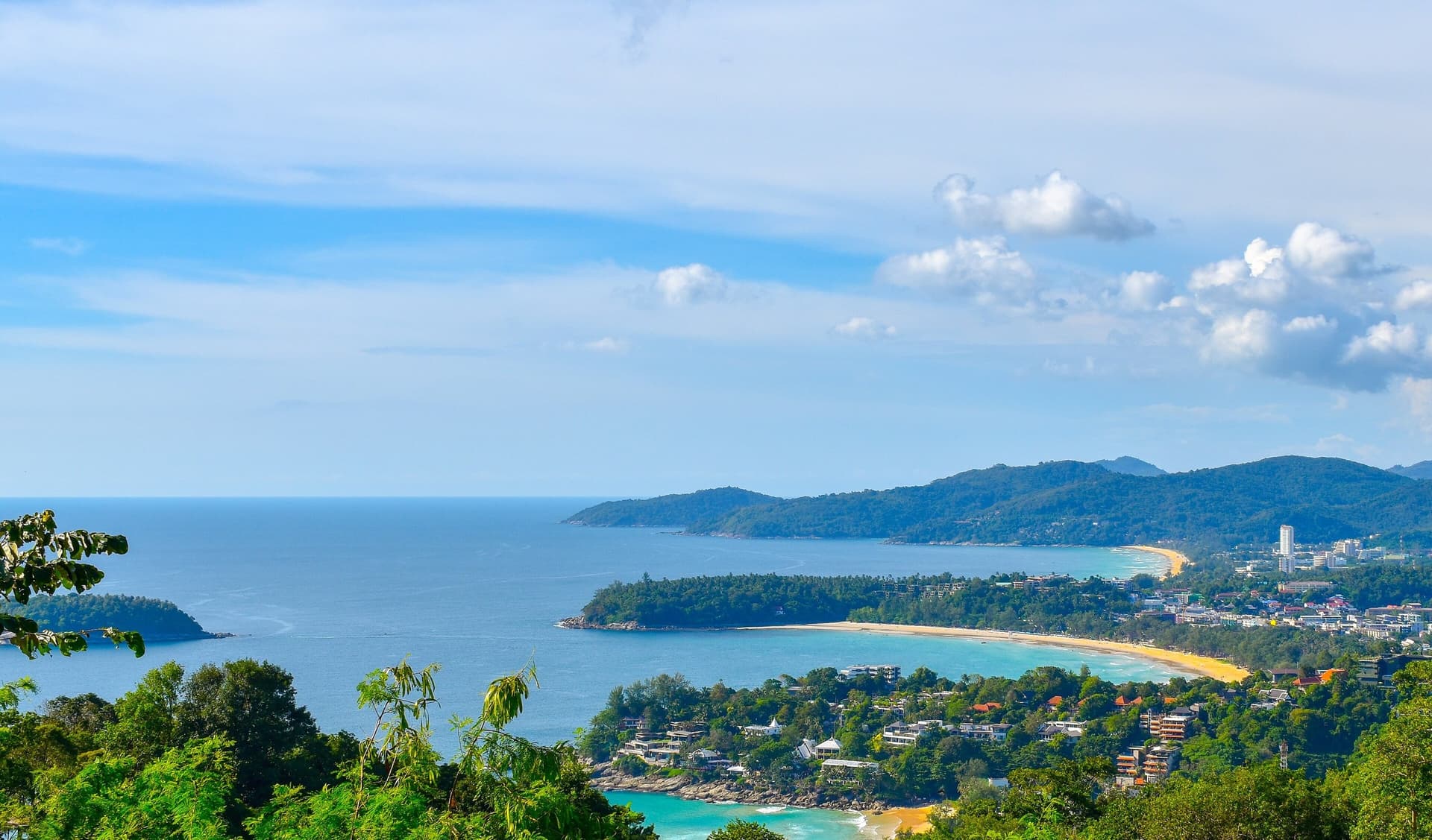 Uitzicht vanaf een groene heuvel op de baaien van Kata Noi, Kata en Karon aan de westkust van Phuket, met turquoise water en blauwe lucht
