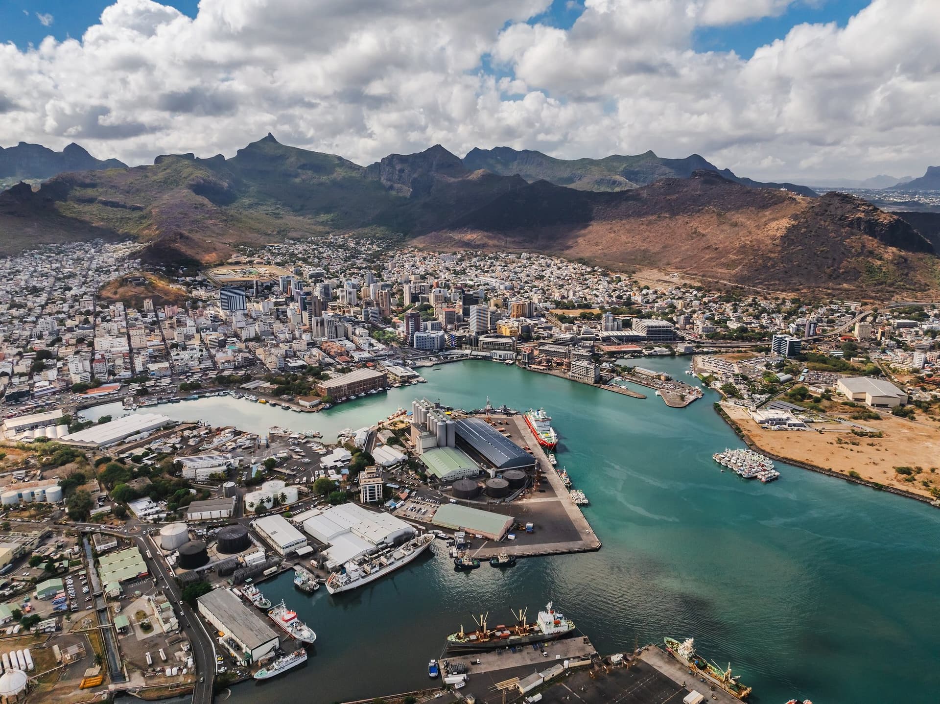 Luchtfoto van Port Louis op Mauritius: de haven met turquoise water, de stad en daarachter een bergketen onder stapelwolken