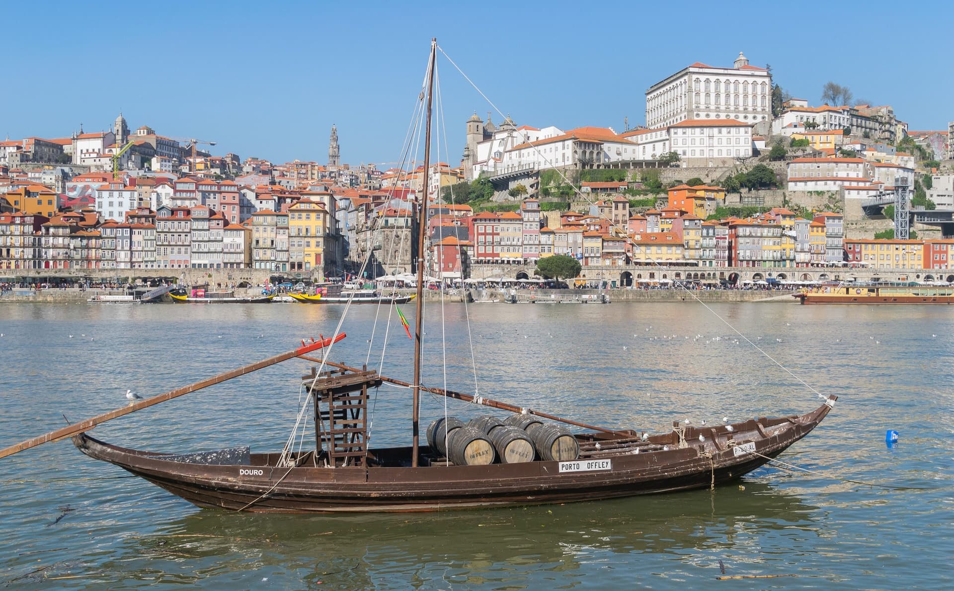 Kleurrijke huizen van de Ribeira in Porto aan de Douro, met een traditionele rabelo-boot op de rivier
