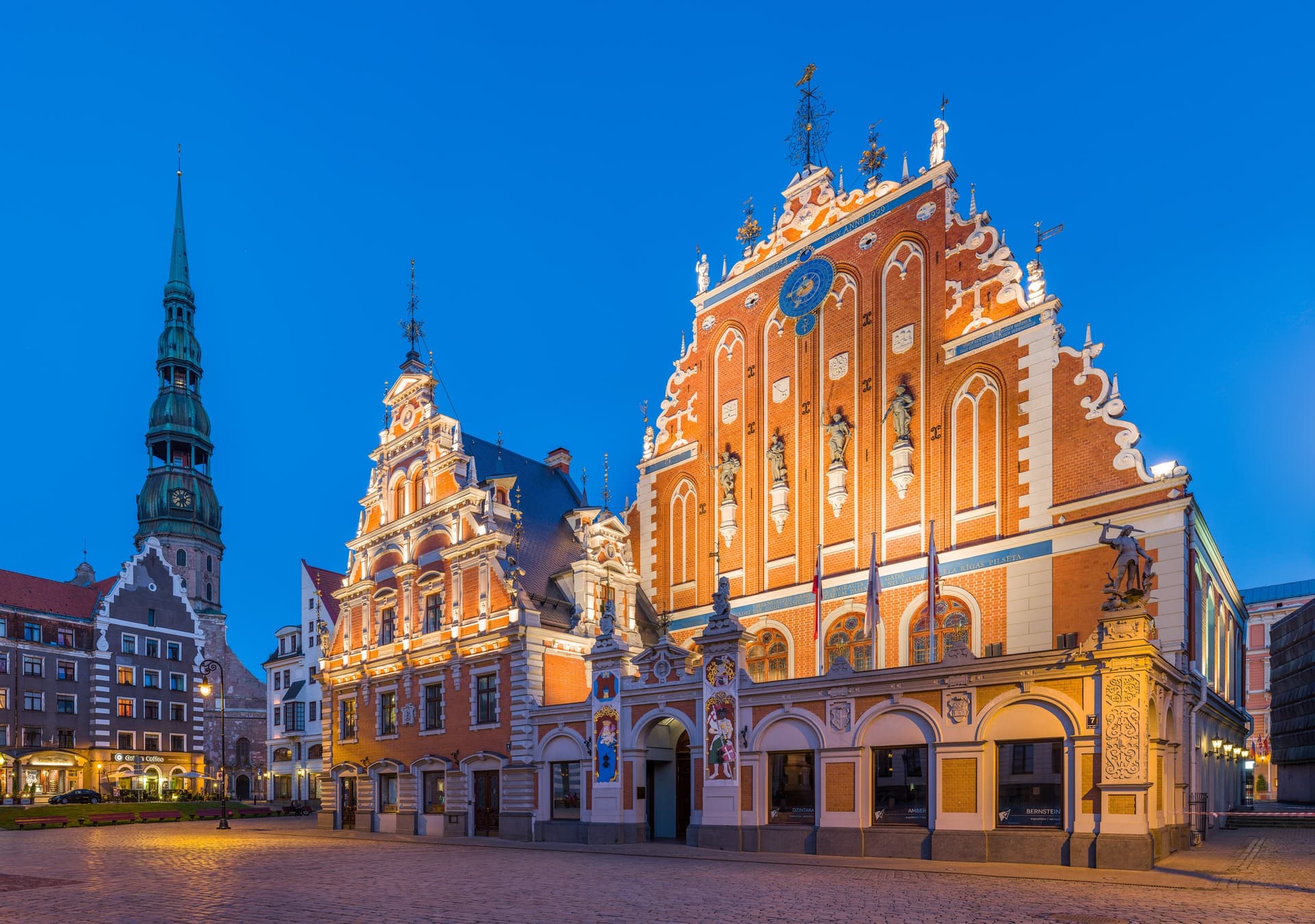 Het verlichte Huis van de Zwarthoofden en de toren van de Sint-Pieterskerk in de oude stad van Riga bij schemering