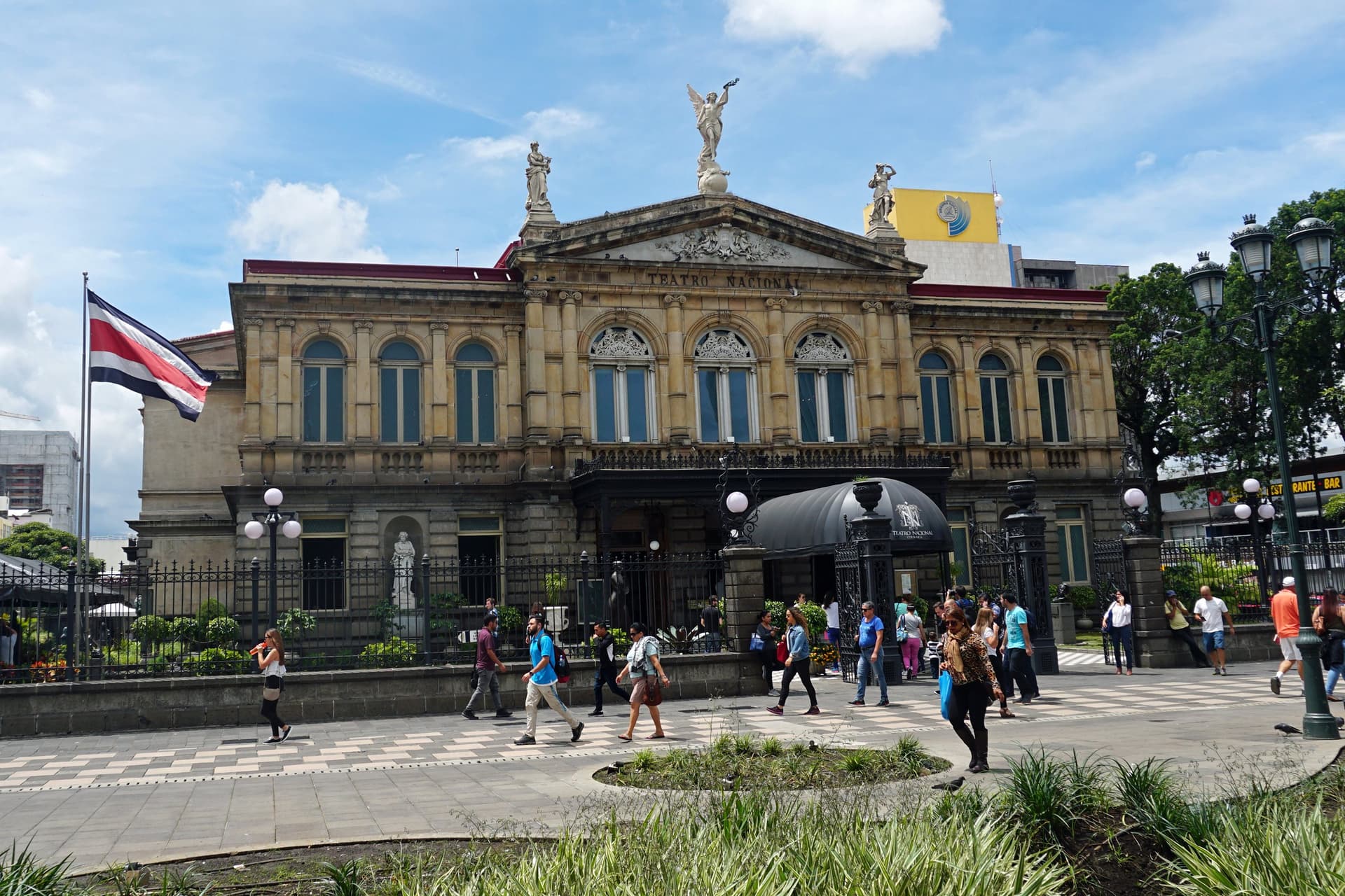 Het neoklassieke Teatro Nacional aan de Plaza de la Cultura in San José, met de Costa Ricaanse vlag en wandelaars op het plein