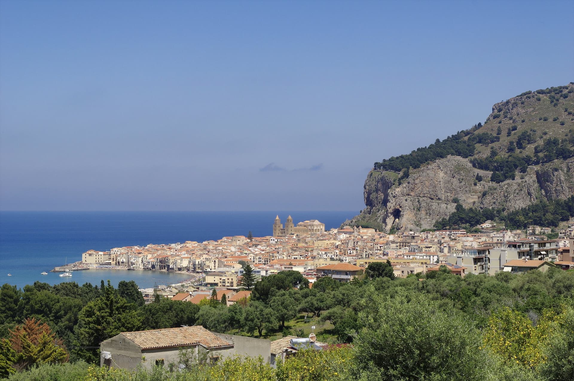 Het kustplaatsje Cefalù op Sicilië met de kathedraal tussen de huizen en de rots La Rocca erachter, aan een blauwe zee