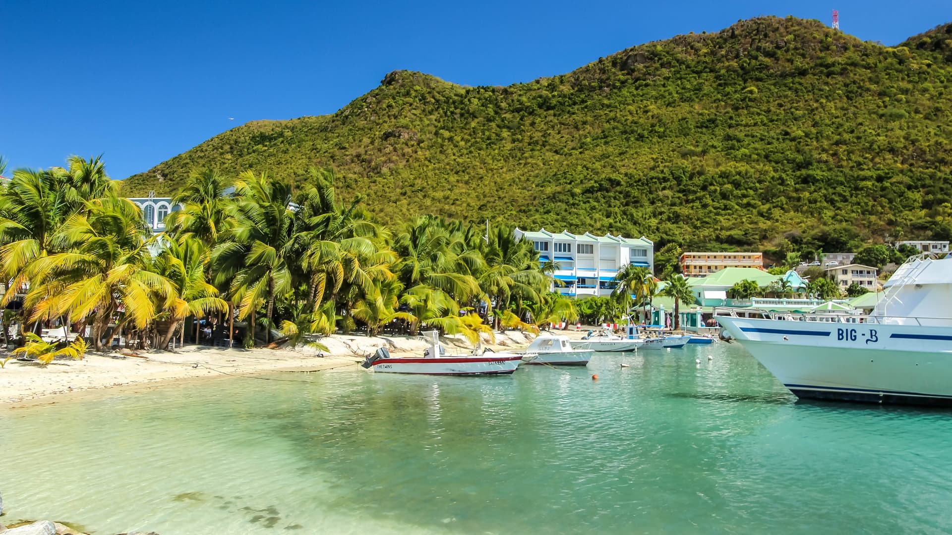 Great Bay Beach in Philipsburg op Sint Maarten met palmbomen, bootjes in helder turquoise water en groene heuvels op de achtergrond